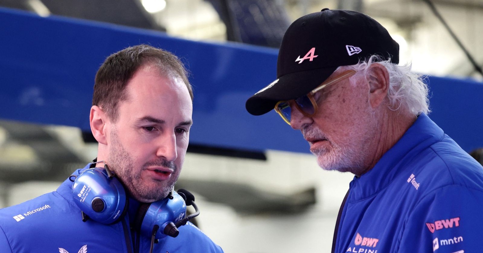 Oliver Oakes und Flavio Briatore im Gespräch in der Alpine-Garage, beide in blauer Teamkleidung mit BWT-Logo.
