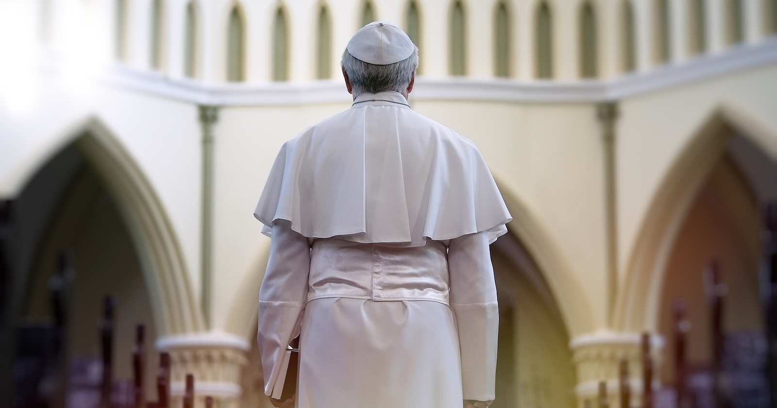 Papst in weißem Gewand von hinten, steht in einer Kirche mit gotischen Bögen, Symbol für das Konklave im Vatikan