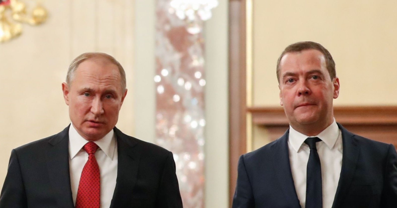 Wladimir Putin und Dmitri Medwedew in Anzug und Krawatte während eines offiziellen Termins im Kreml, ernster Gesichtsausdruck vor prunkvollem Hintergrund.