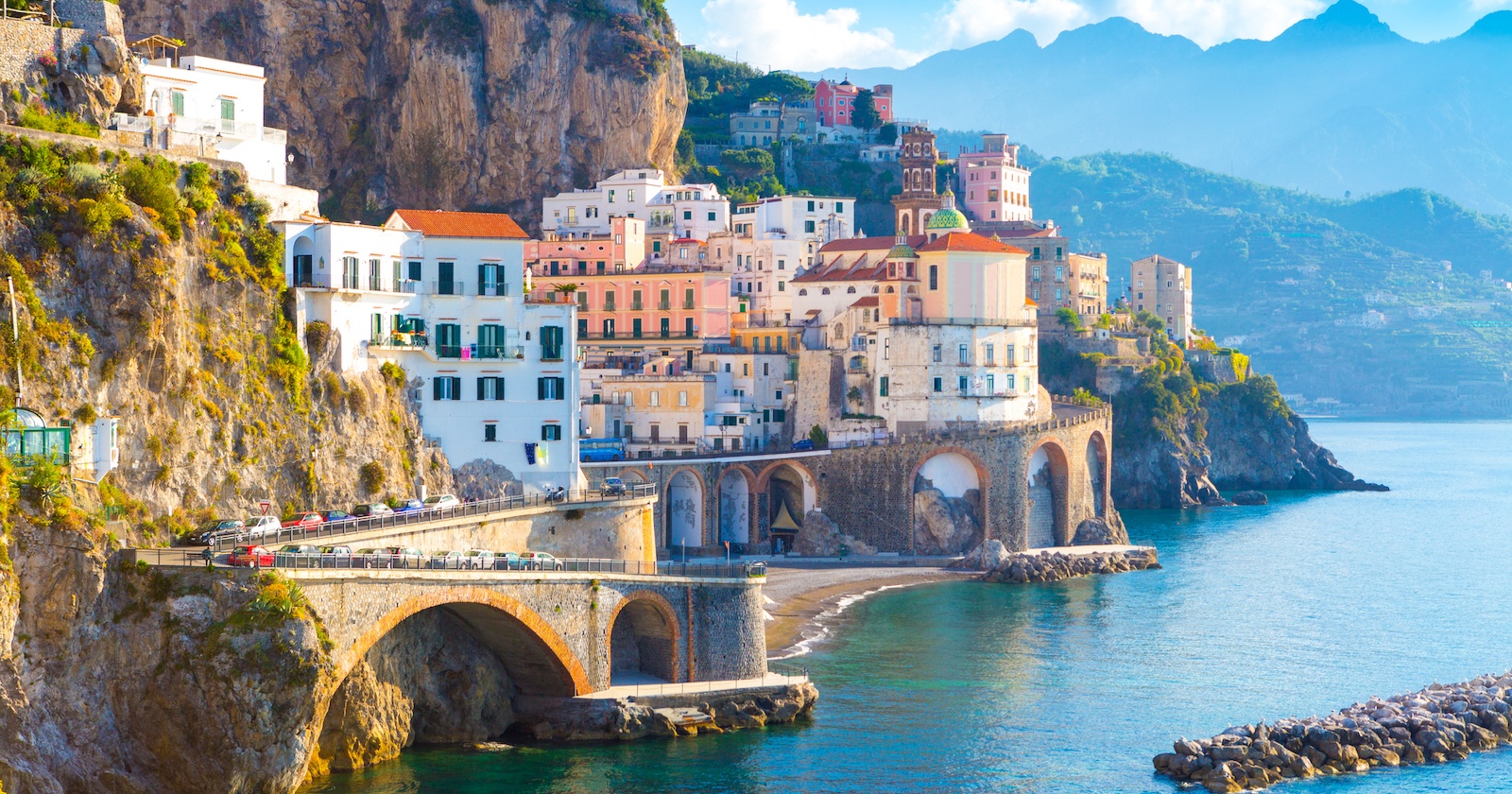 Panoramablick auf die farbenfrohen Häuser der Amalfi-Küste in Italien, eingebettet in steile Felsklippen am Meer mit türkisblauem Wasser und Küstenstraße.