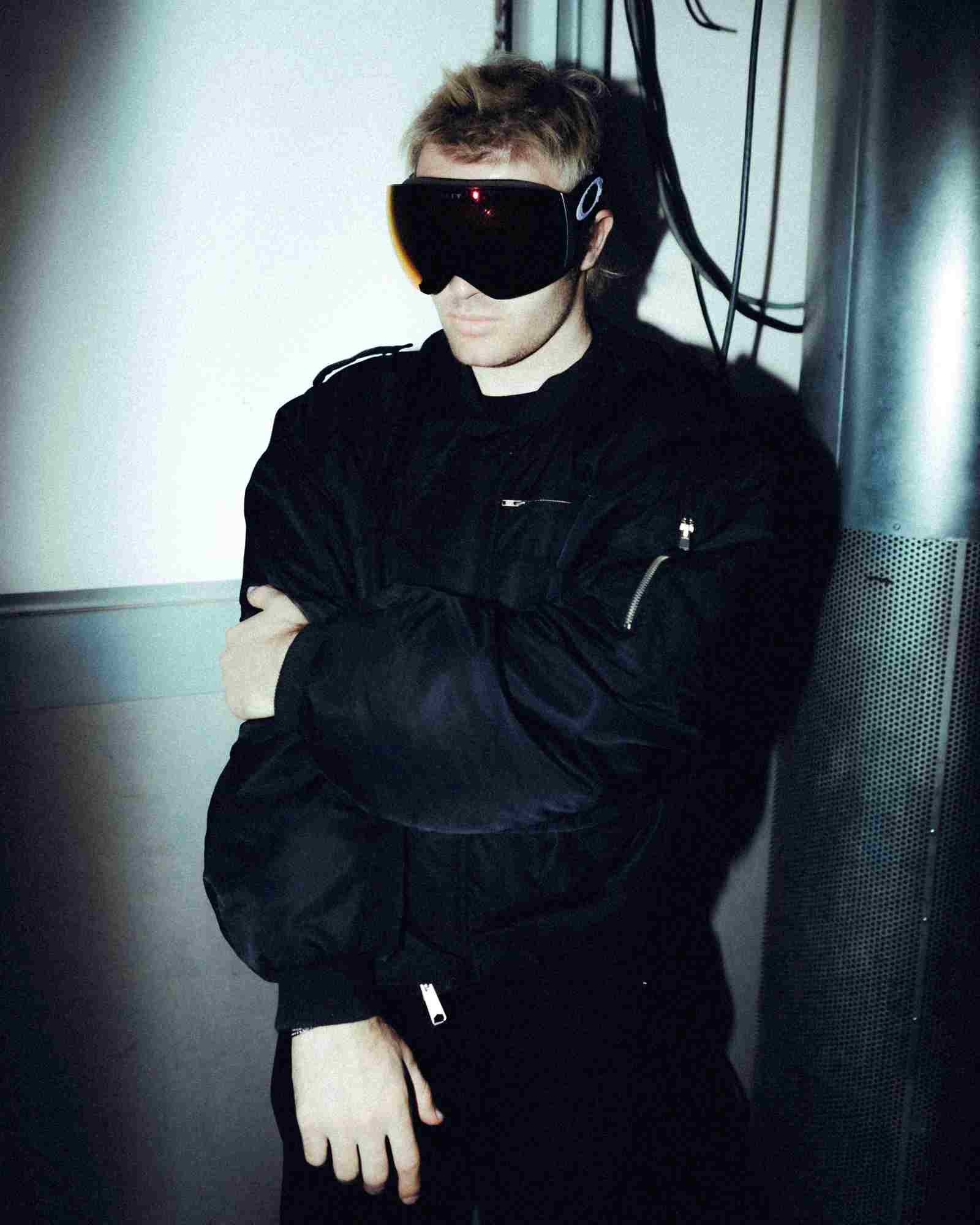 Der deutsche Rapper Ski Aggu, komplett schwarz gekleidet mit einer Skibrille (seinem Markenzeichen). Der Hintergrund ist grau, schwarz.