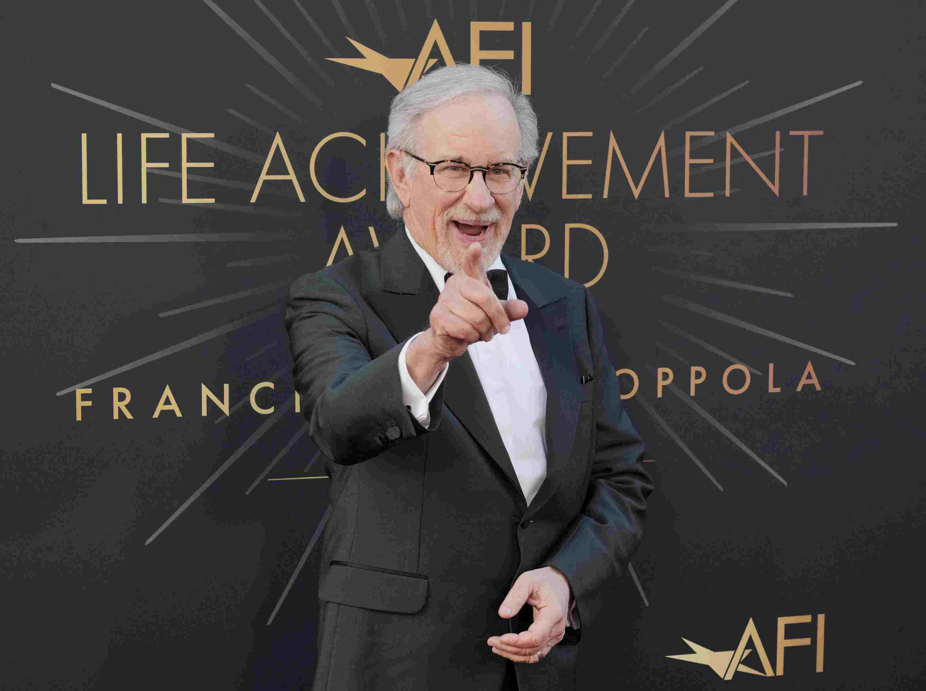 Steven Spielberg im Smoking, er lächelt und deutet mit dem Zeigefinger in Richtung Kamera.