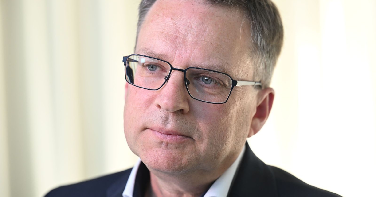 Porträt von August Wöginger, der eine Brille trägt und ernst in die Kamera blickt.