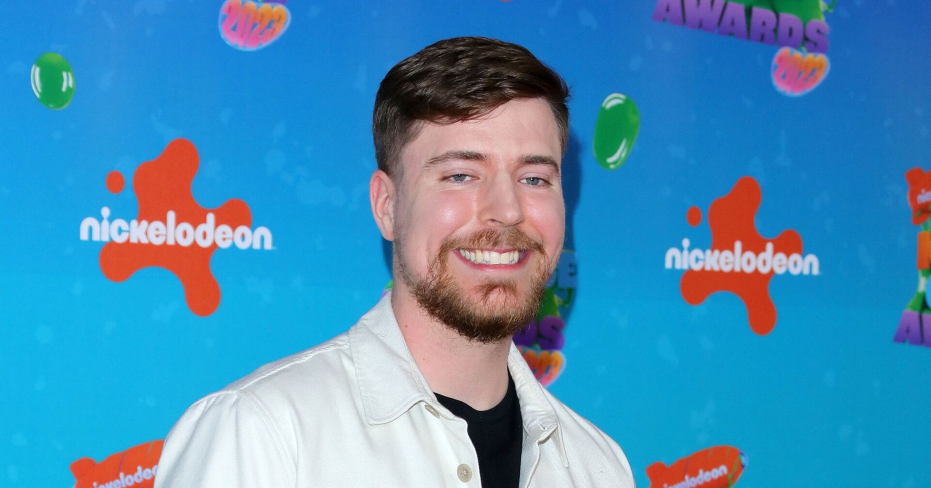 YouTube-Star MrBeast steht lächelnd vor einer blauen Wang