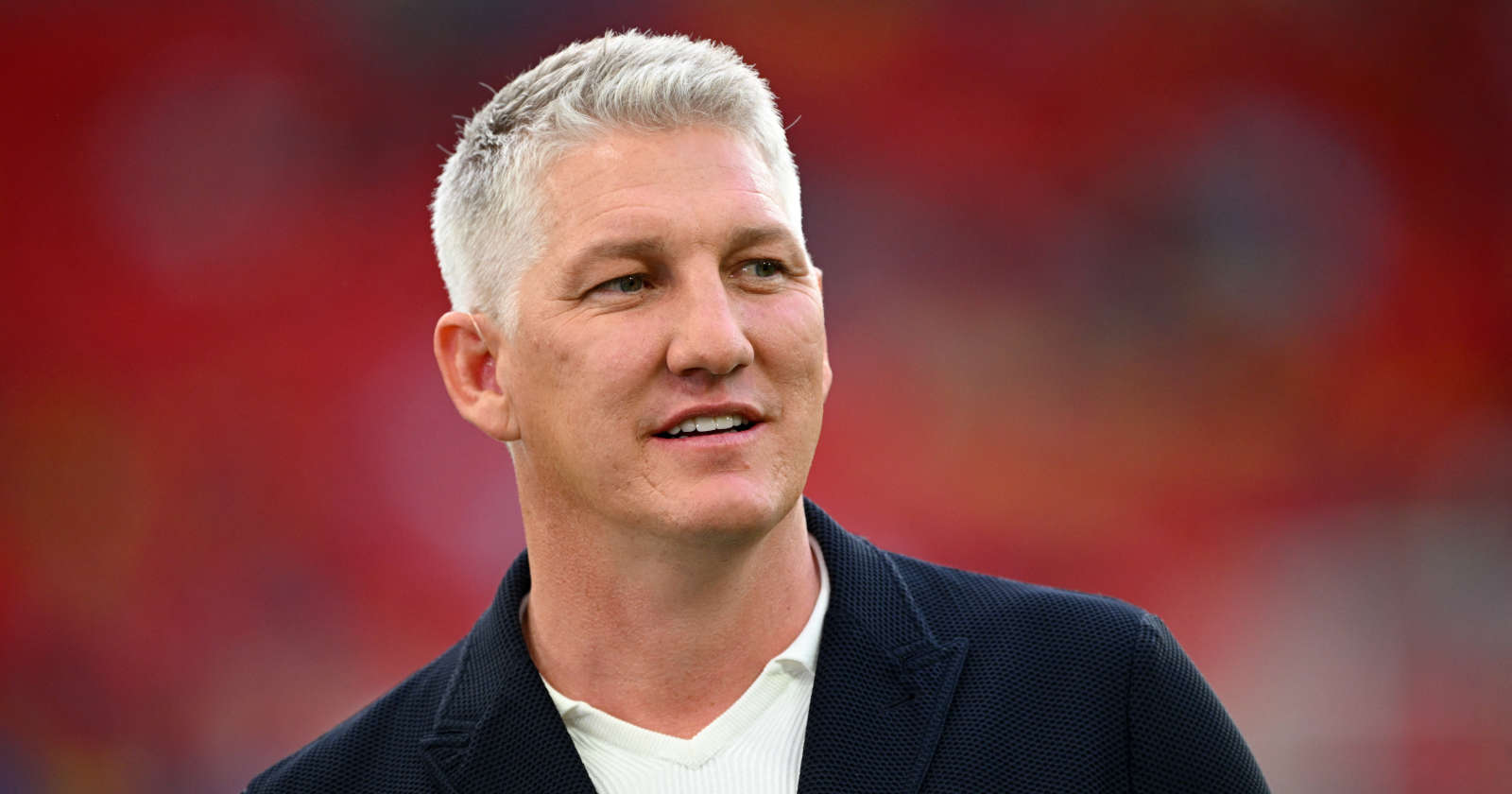 Bastian Schweinsteiger lächelnd im Porträt vor verschwommenem Hintergrund.