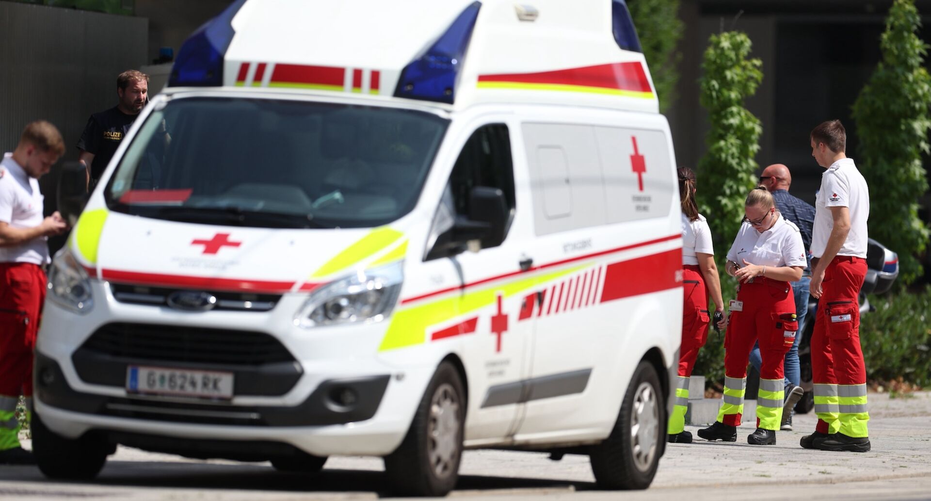 Sanitäterinnen und Sanitäter des Roten Kreuzes sowie Polizeibeamte stehen neben einem Rettungswagen im Einsatzgebiet nach dem Amoklauf in Graz.