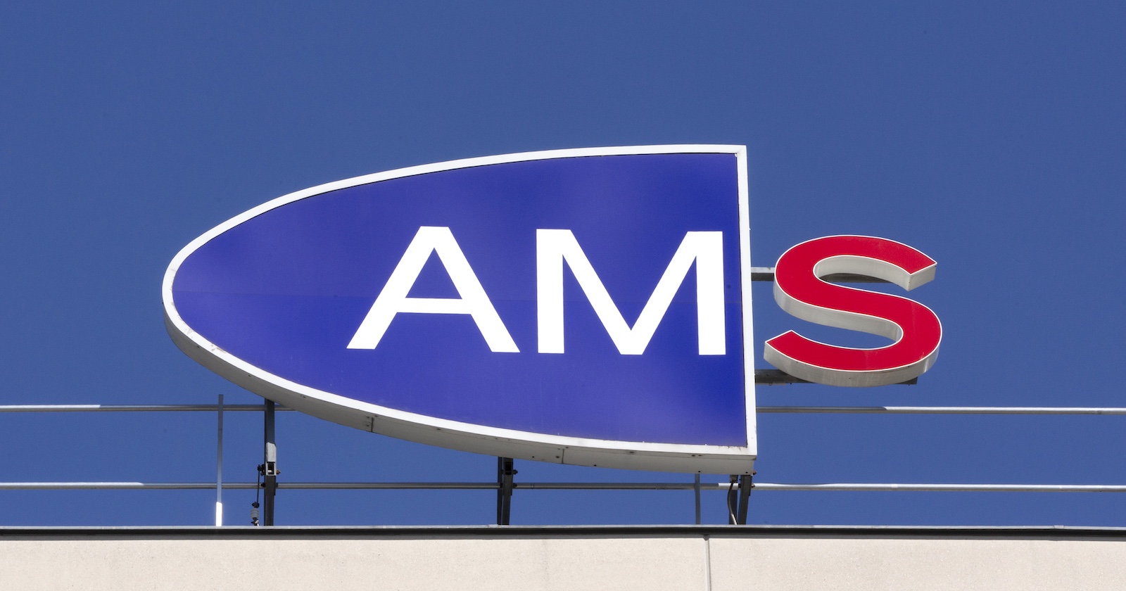 Logo des Arbeitsmarktservice (AMS) auf einem Gebäudedach vor blauem Himmel, das rote S am rechten Rand leuchtet.
