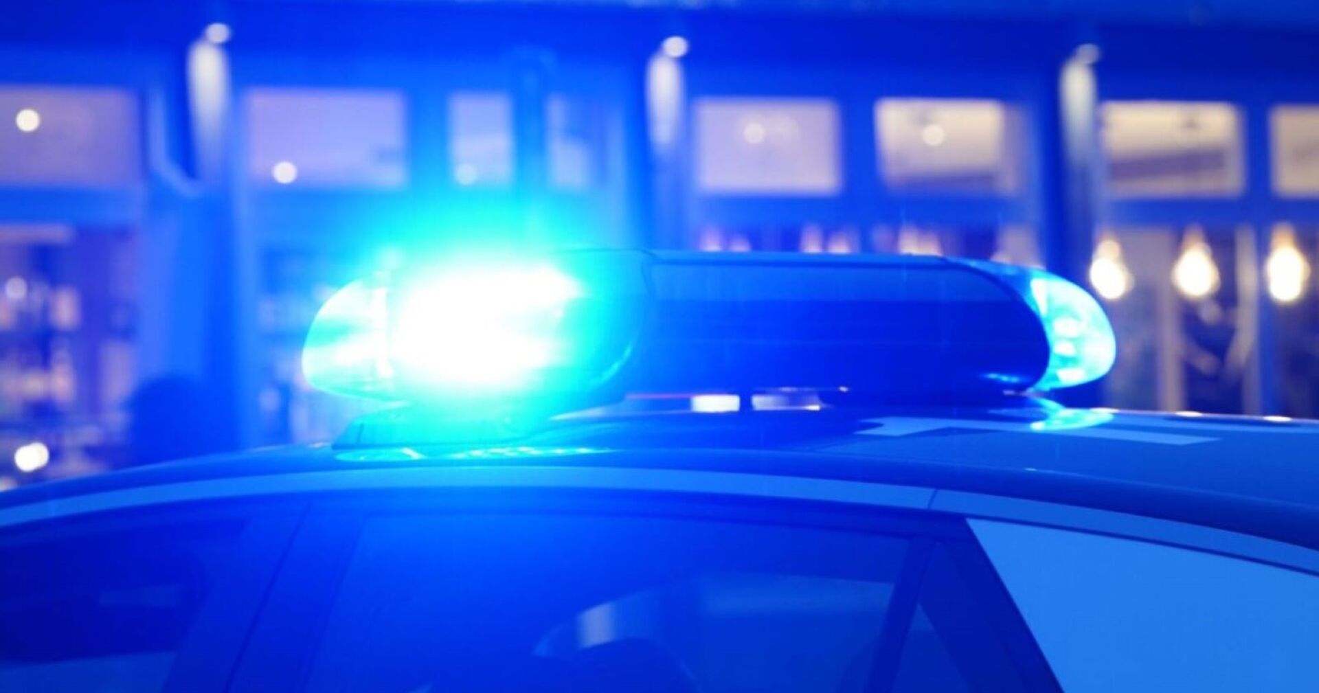 Polizeiauto mit eingeschaltetem Blaulicht vor unscharf beleuchtetem Hintergrund bei Nacht.