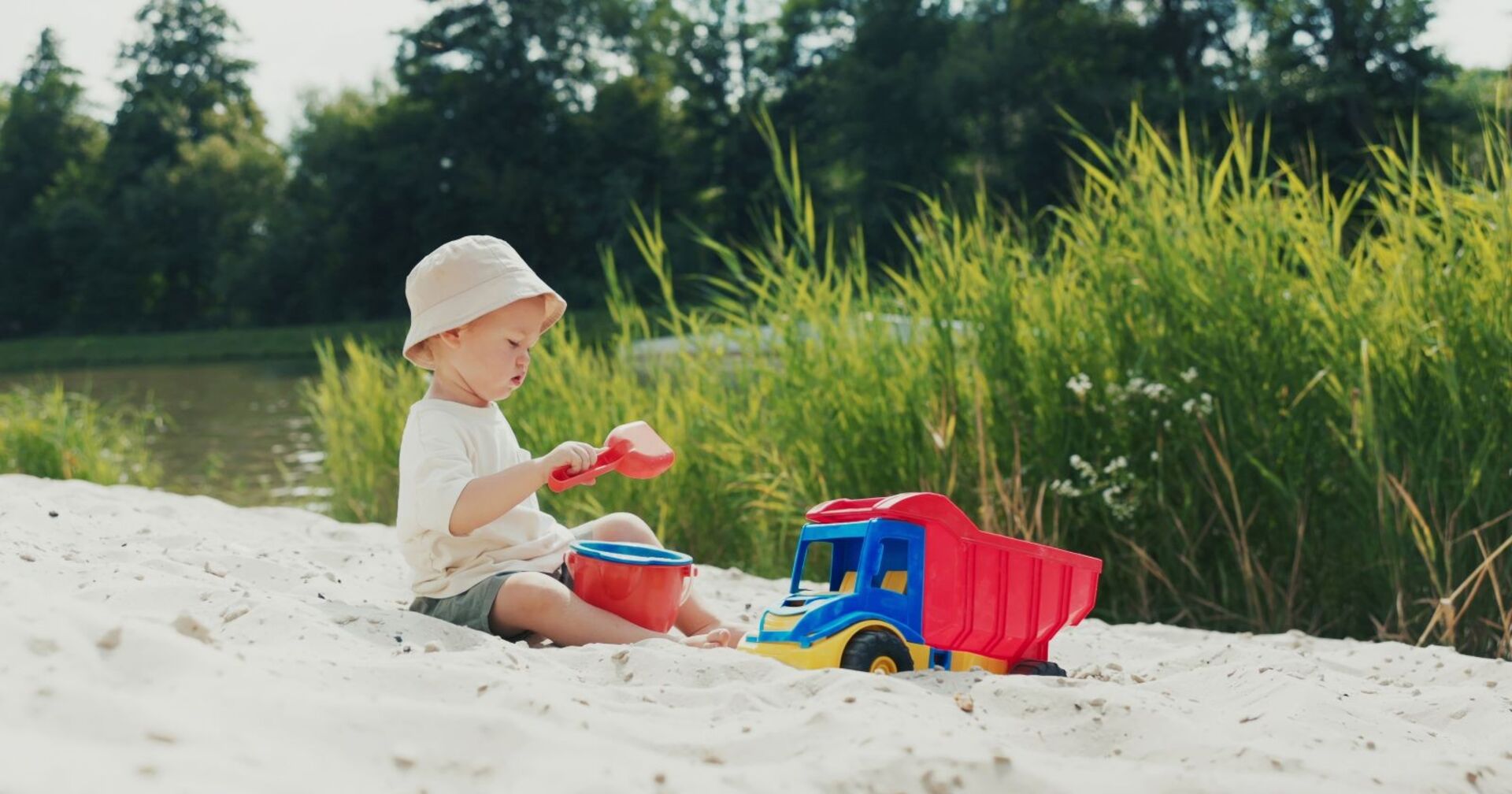 Am Strand spielt ein Junge mit Hut im Sandkasten, schaufelt Sand in einen Eimer und genießt die Natur