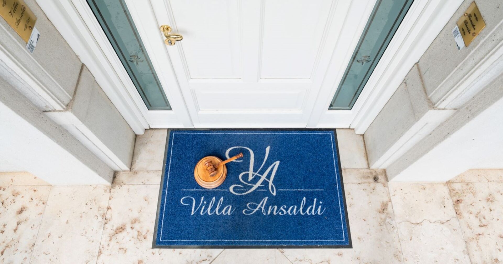 Eingangsbereich der Villa Ansaldi mit blauer Fußmatte und Auktionshammer – Aufnahme aus der Vogelperspektive.