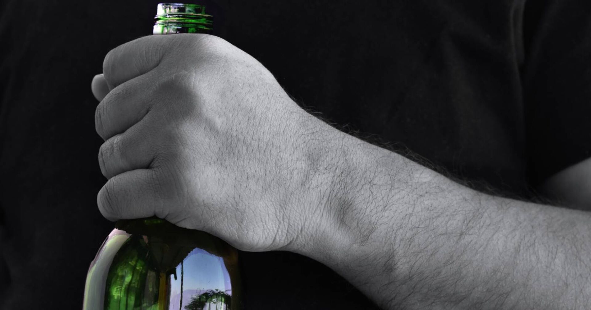 Nahaufnahme einer Hand, die den Hals einer Bierflasche umklammert