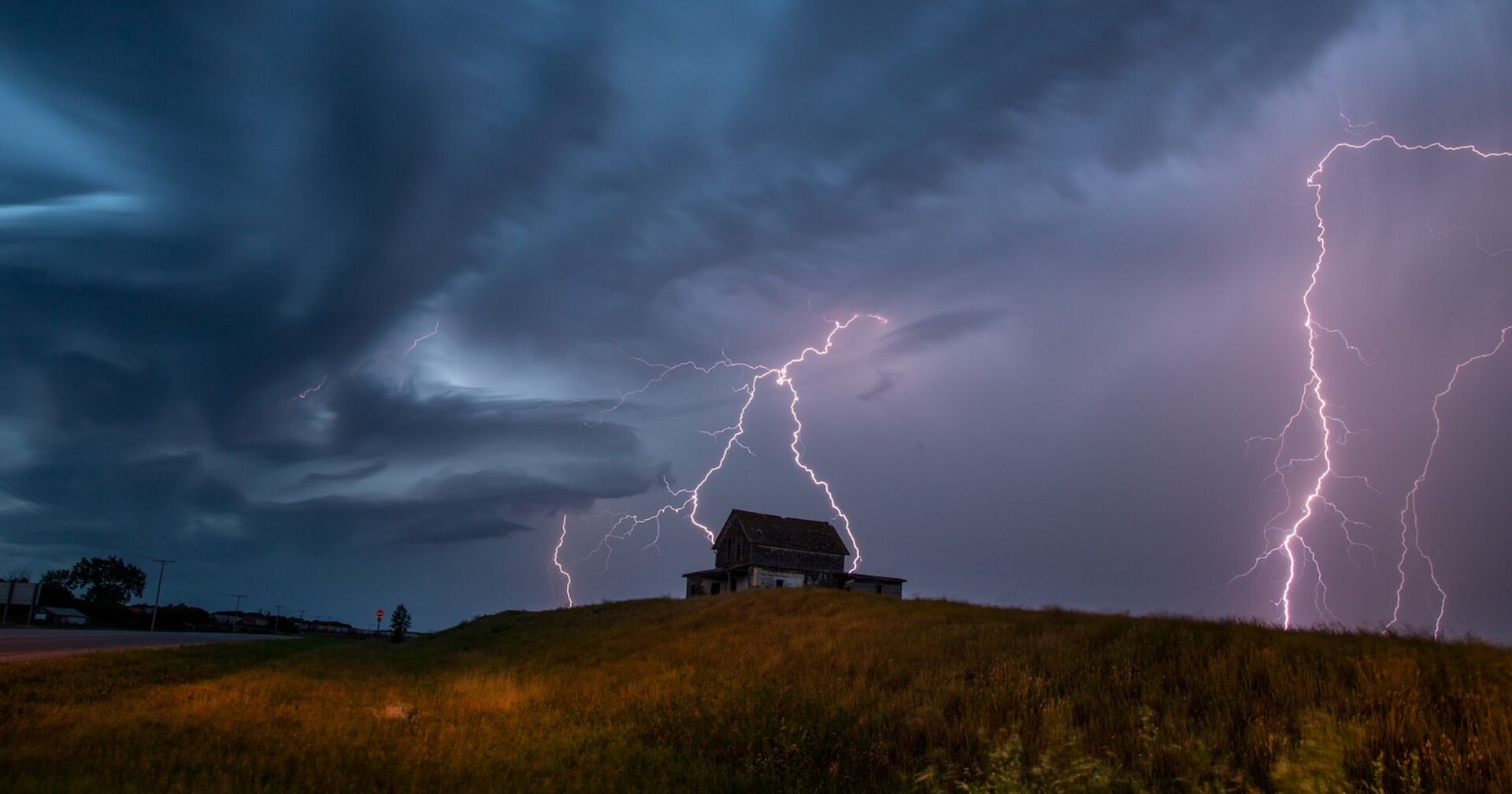 Blitzeinschlag in Haus auf einer Alpe bei Nacht, dunkle Gewitterwolken und mehrere grelle Blitze am Himmel.Ein Blitz schlägt während eines schweren Gewitters in ein Gebäude auf einer Alpe ein.