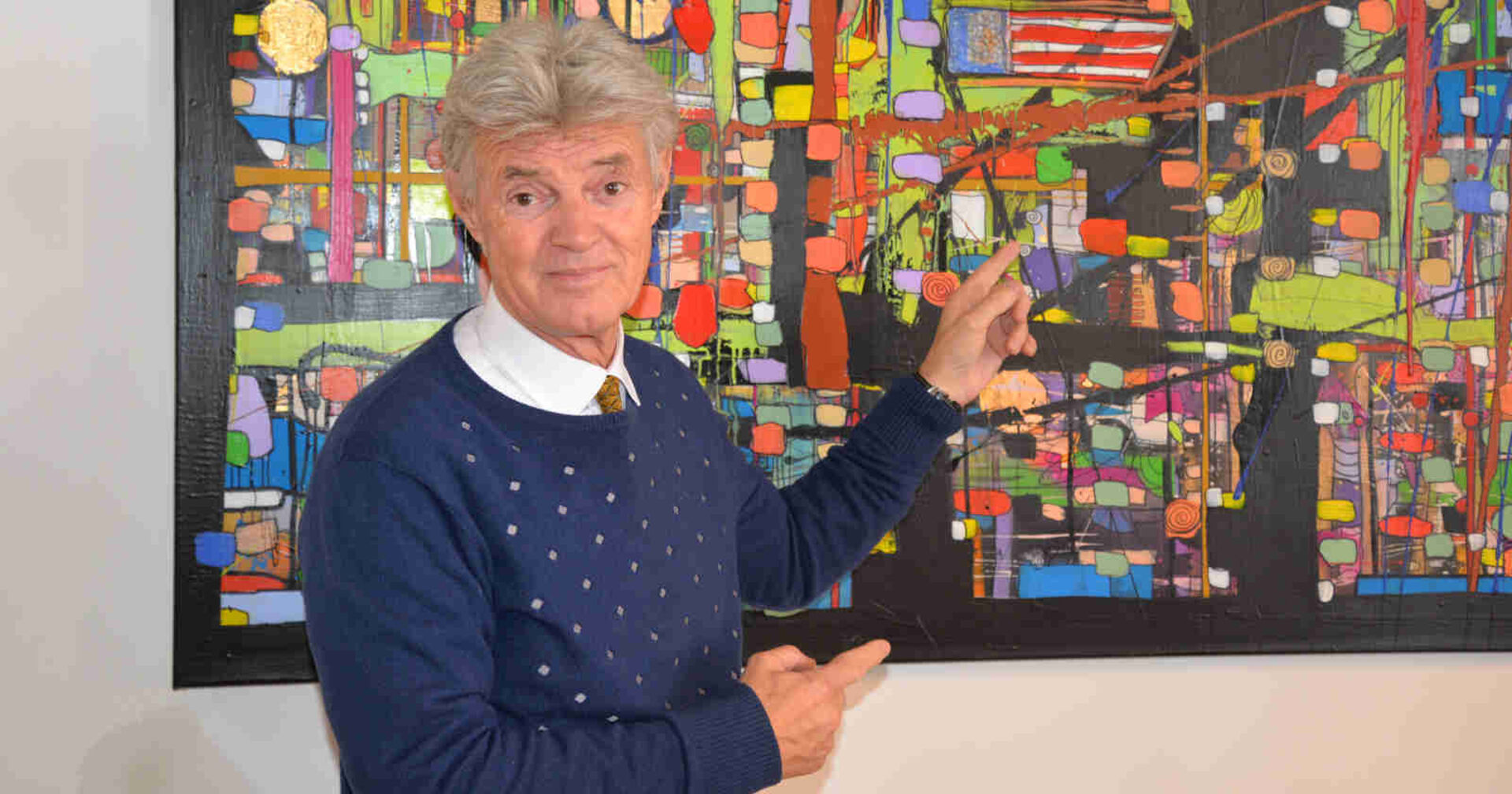 Mann zeigt auf ein Bild, das hinter ihm hängt