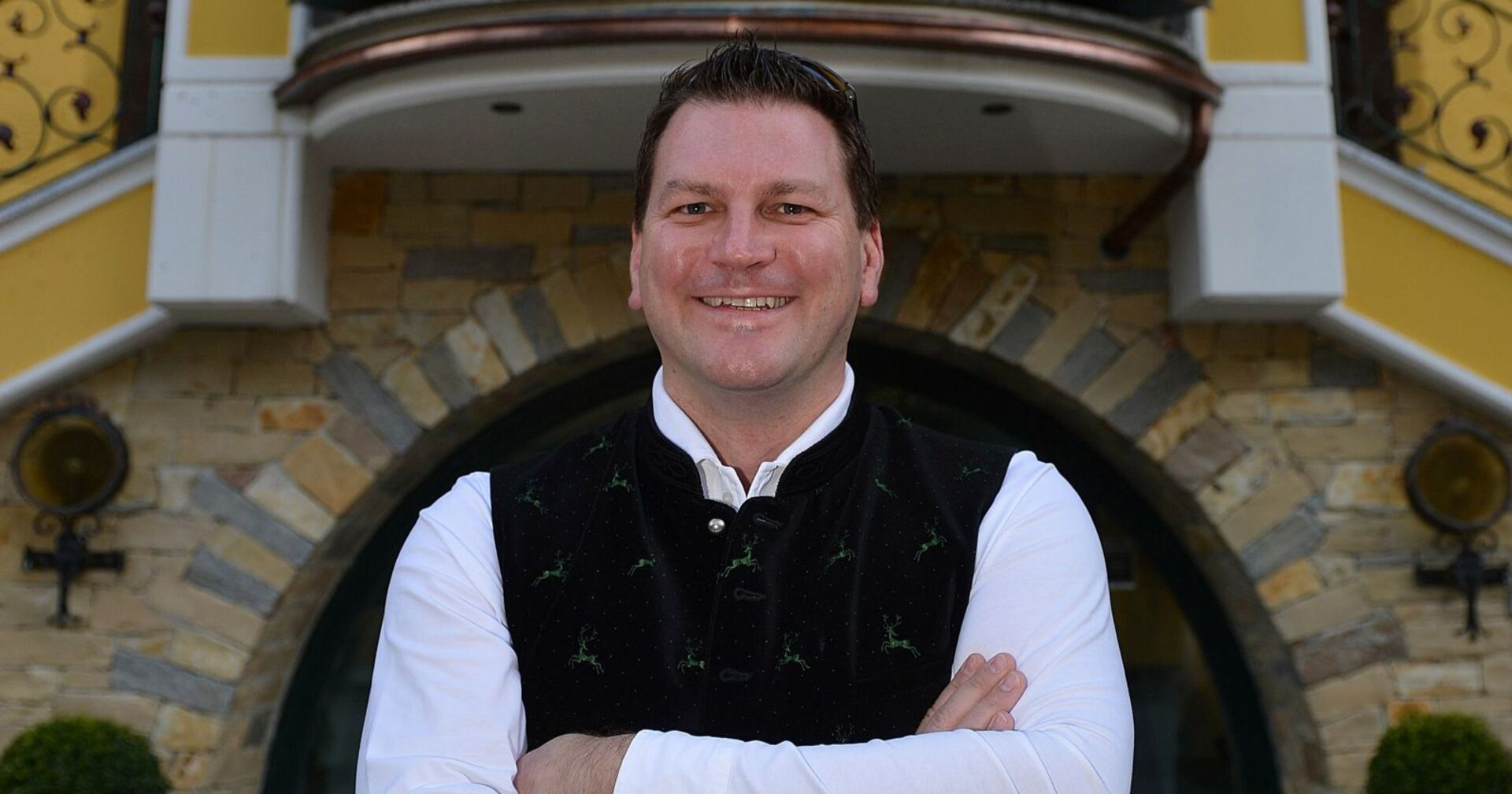 Hotelier Christian Steiner steht lächelnd mit verschränkten Armen vor seinem Hotel