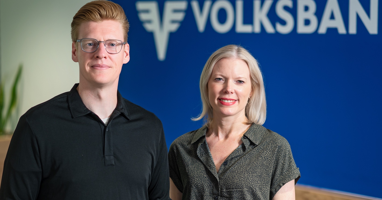 Mann mit Brille und schwarzem Shirt und Frau mit Bluse im Printlook vor einer blauen Wand