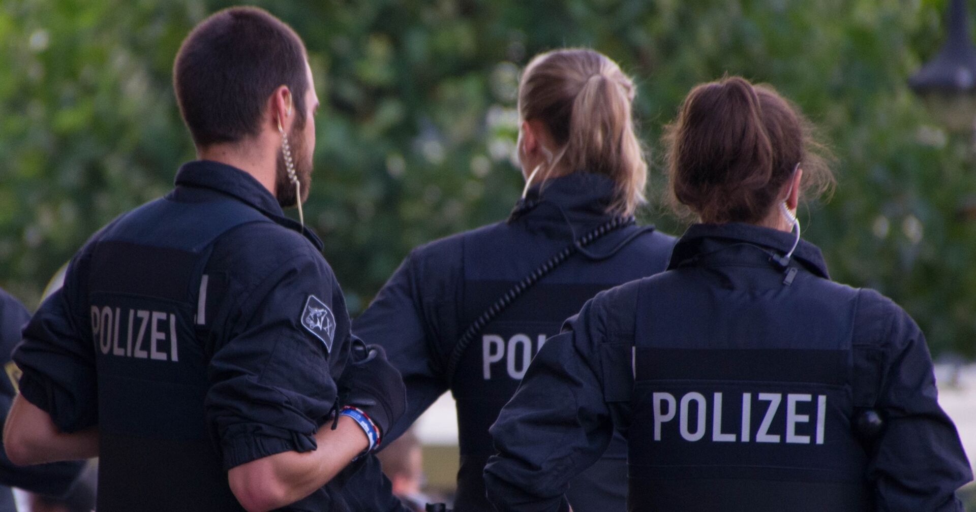 Drei Polizist:innen von hinten in Einsatzkleidung bei einem Einsatz im Freien