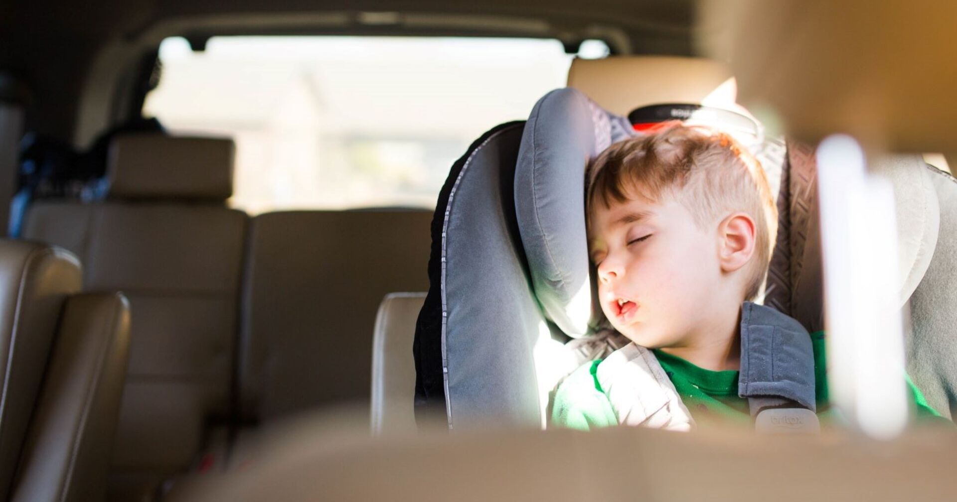 Kind schläft im Kindersitz im Auto, Sonne scheint herein, Gefahr durch Hitze und Überhitzung für Kinder im geparkten Auto.