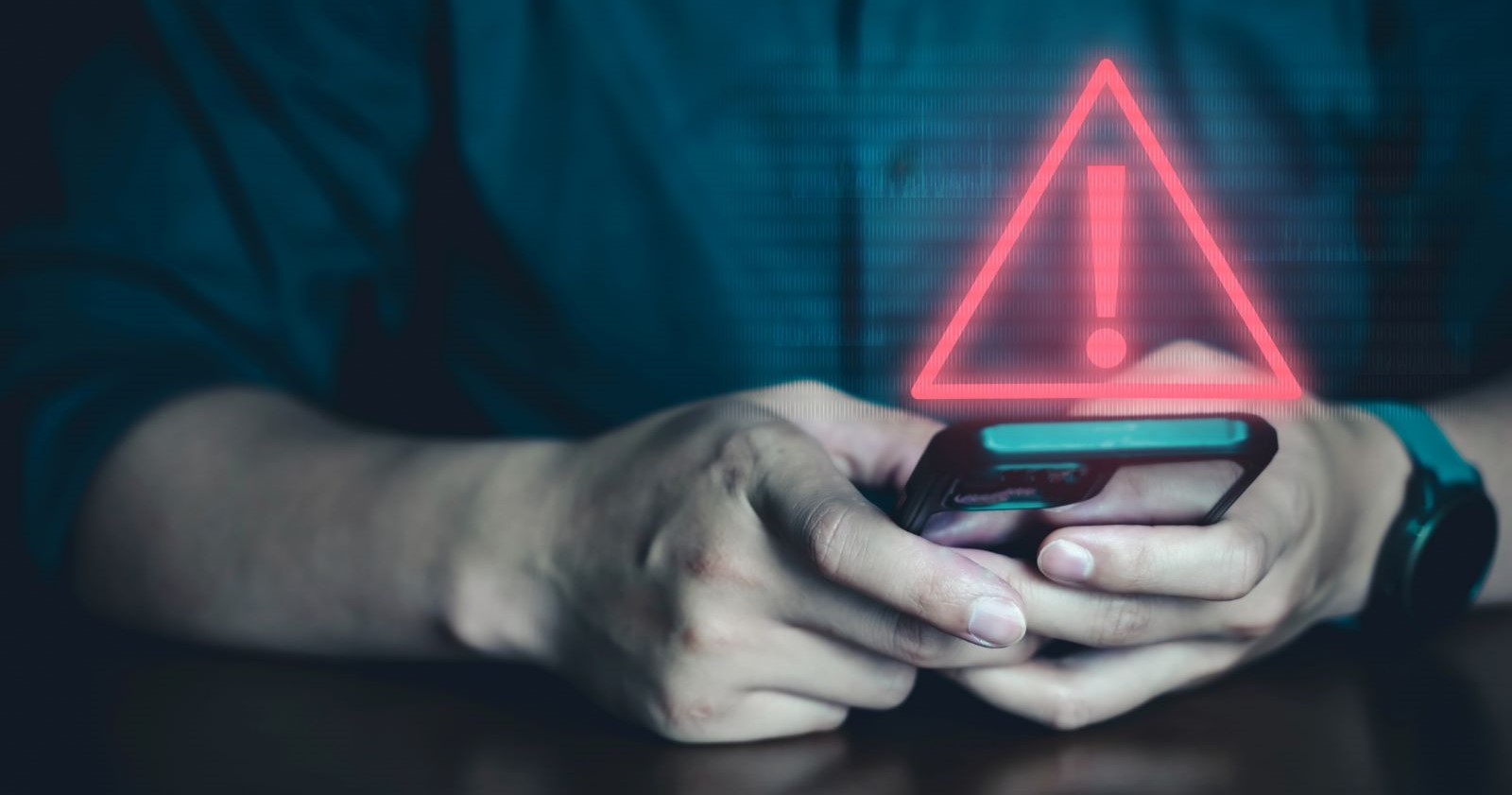 Person hält ein Smartphone in der Hand, darüber ein eingeblendetes rotes Warnsymbol mit Ausrufezeichen – Symbolbild für eine Sicherheitswarnung.