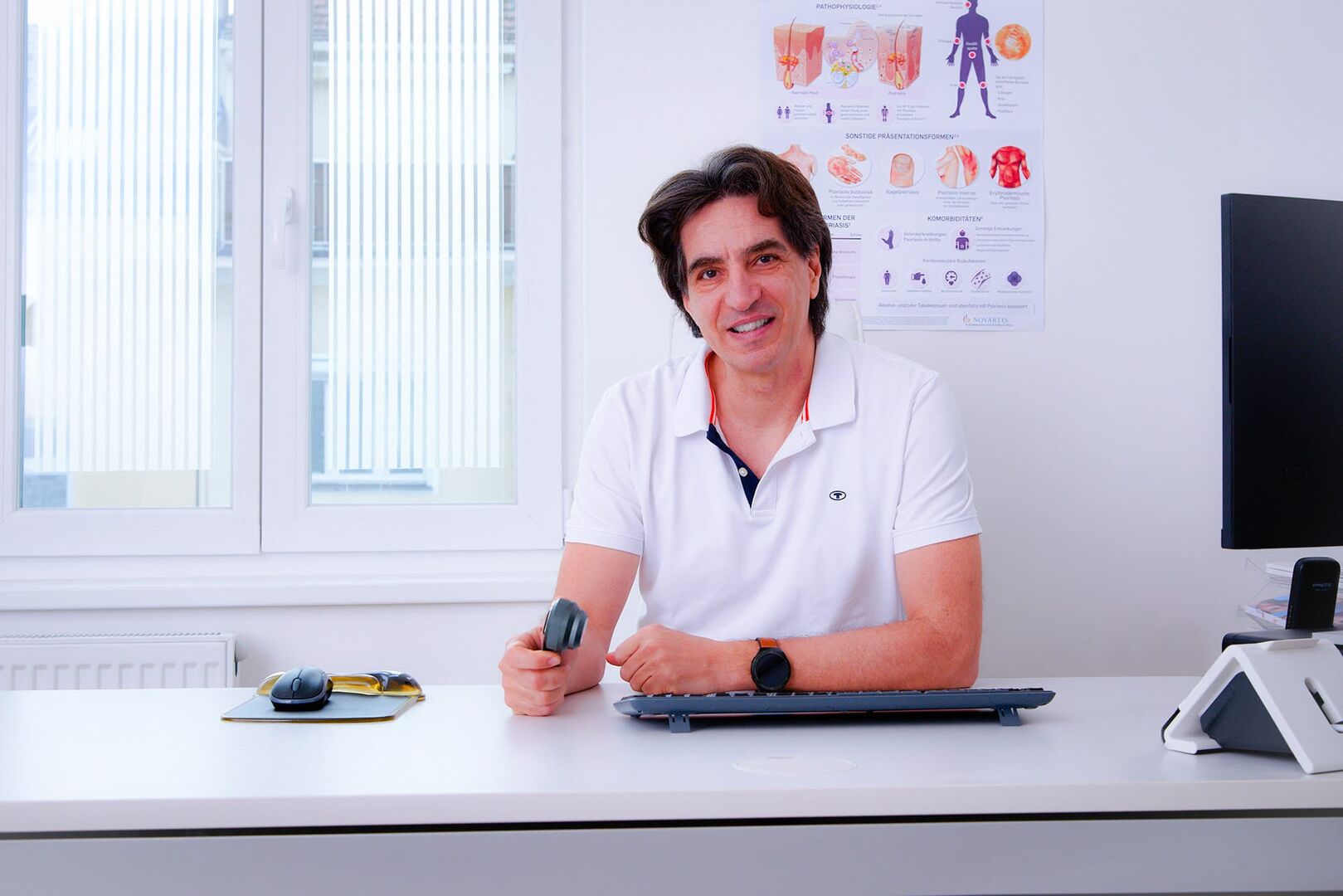 Der Wiener Hautarzt Andreas Tzovaras, der in seiner Praxis hinter einem Schreibtisch sitzt