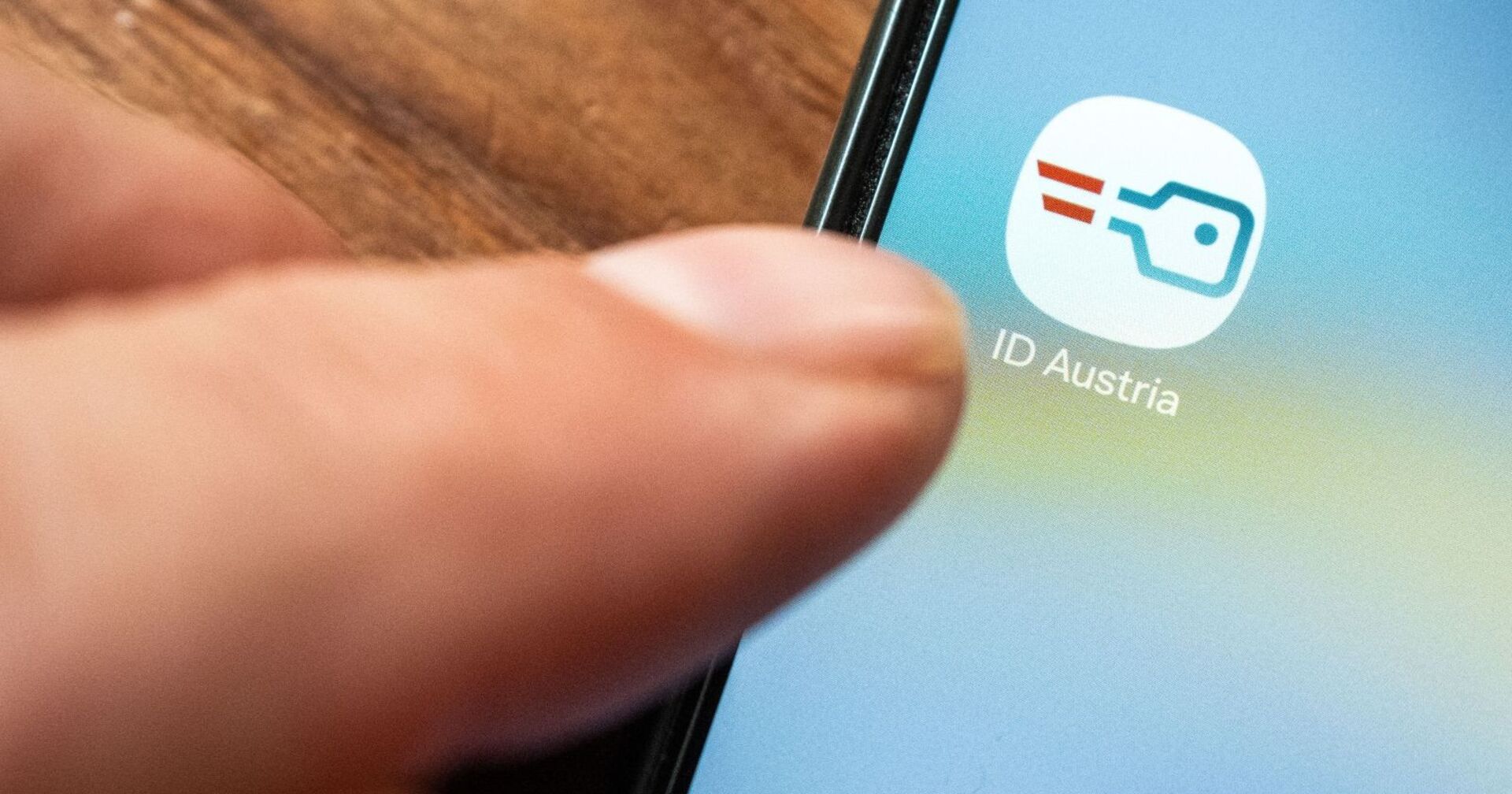 Smartphonedisplay, welches die &quot;ID Austria&quot; App anzeigt, Ein Finger klickt darauf