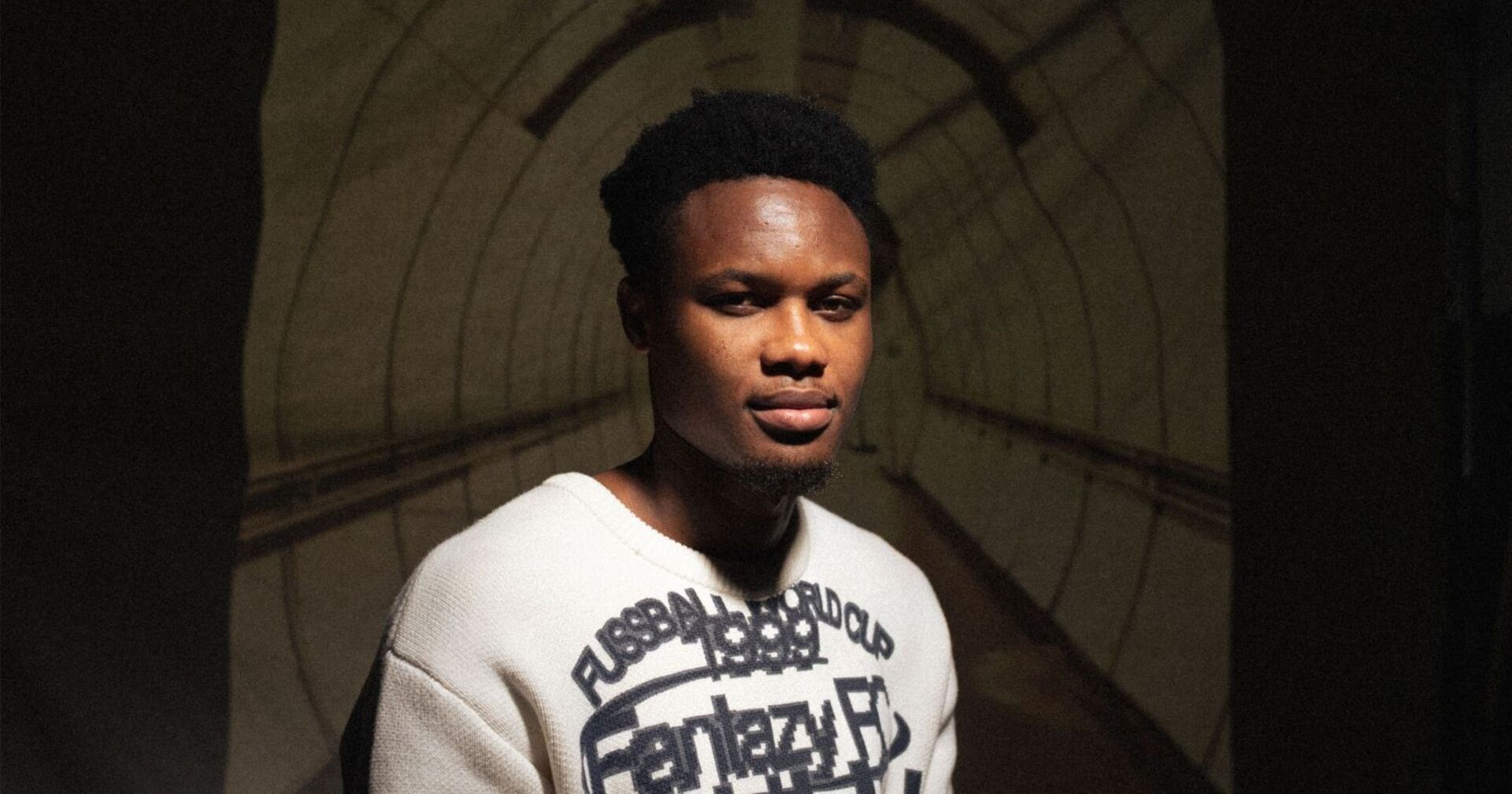 Kelvin Boateng vor einer Leinwand sitzend, welche den Durchgang der U-Bahn-Station Altes Landgut zeigt