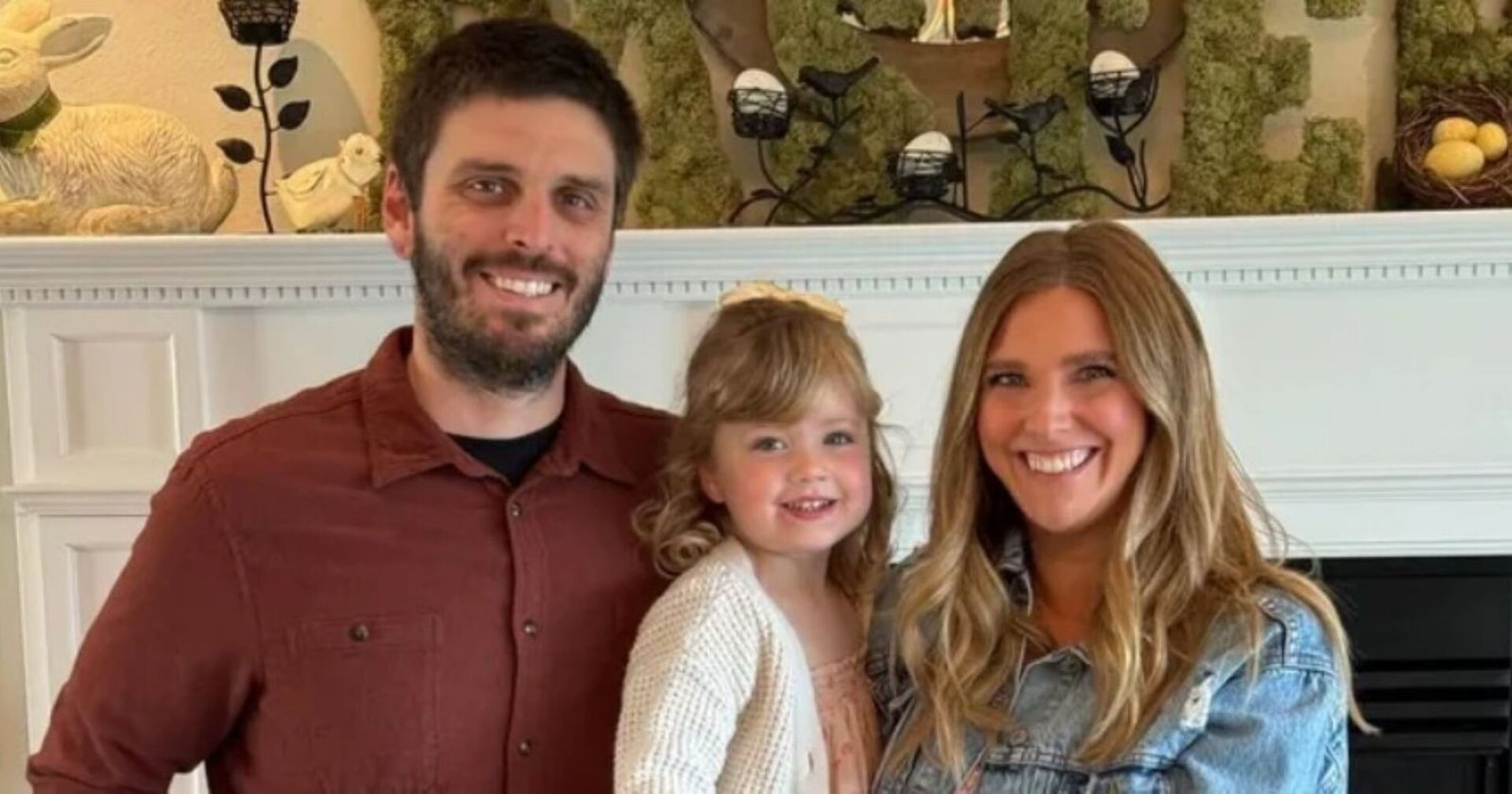 Lauren Miller mit ihrer Familie – Ehemann Kevin Miller und Tochter Emma vor einem Kamin, beide Eltern lächeln in die Kamera.