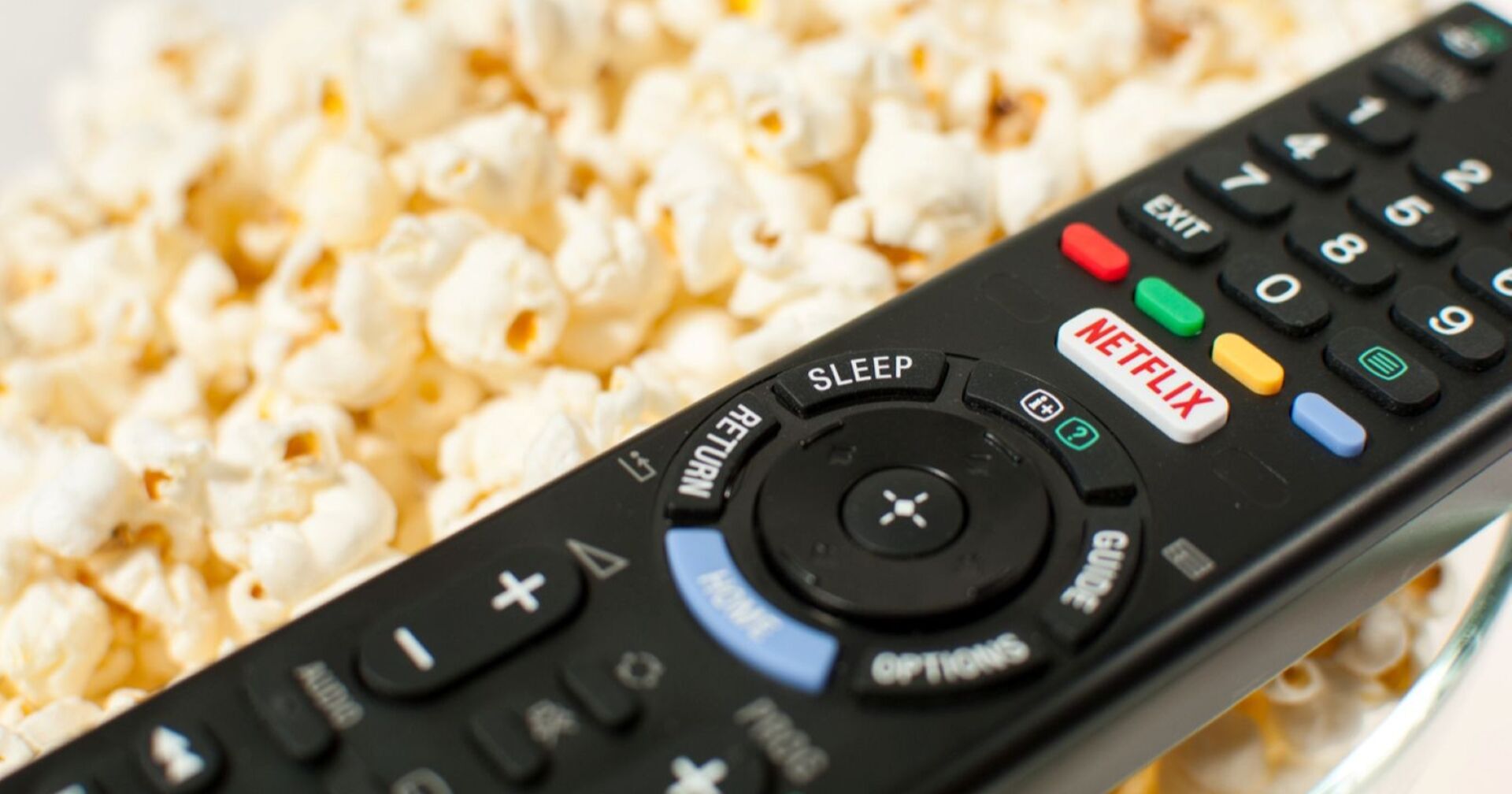 schwarze Fernbedienung mit weißem Netflix-Knopf mit roter Aufschrift &quot;Netflix&quot;, liegt auf Popcorn