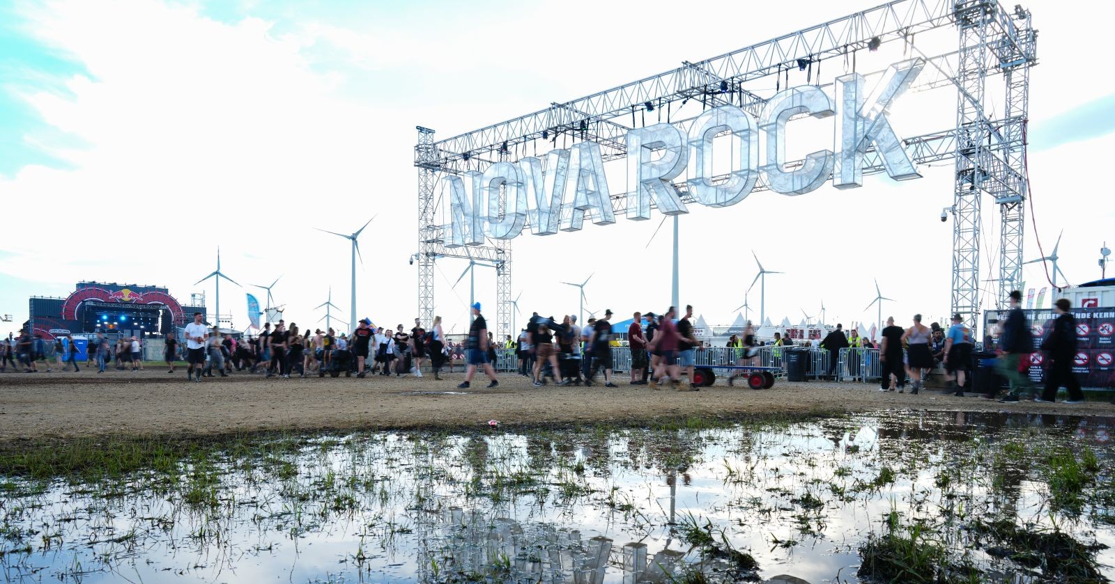 Nova Rock-Festivalgelände mit kleinem Gewässer und Eingangspforte mit Aufschrift &quot;Nova Rock&quot; und Menschen