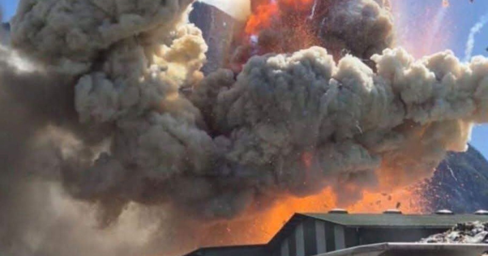 Explosion mit riesiger Rauch- und Feuerwolke über Industriegebäuden in Nußdorf-Debant, dahinter Berge, dramatische Szene während eines Großbrands.