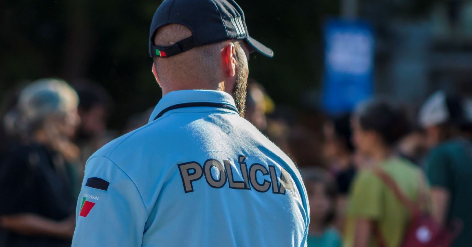 Polizist von hinten im Einsatz, er trägt eine blaue Uniform und eine dunkle Kappe