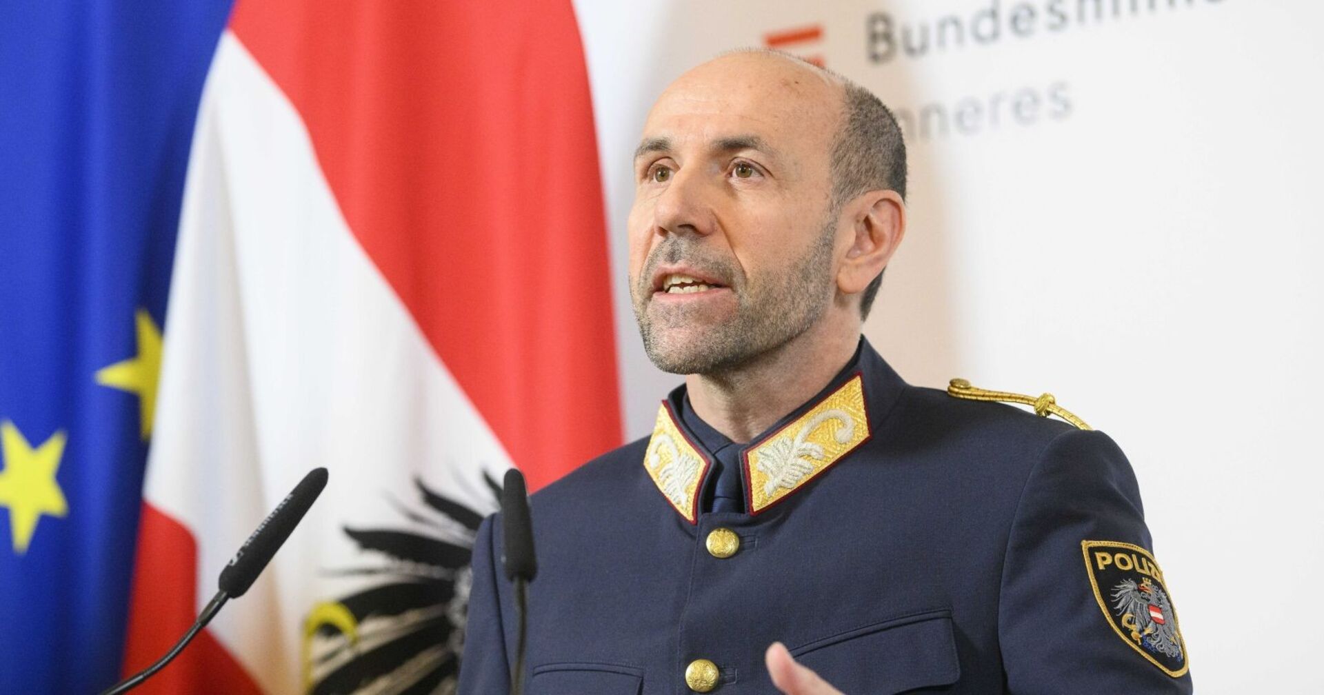 Franz Ruf in Uniform bei einer Pressekonferenz, im Hintergrund österreichische und EU-Flagge.