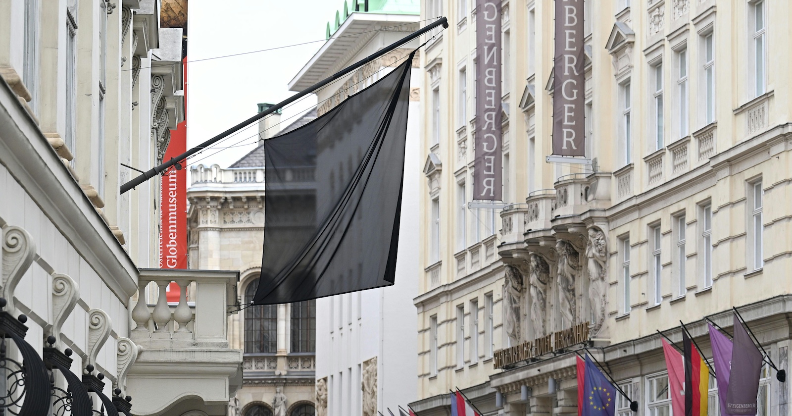 Schwarze Trauerfahne weht vor dem Globenmuseum in der Wiener Innenstadt. Rechts im Bild Hotel Steigenberger, mehrere Nationalflaggen, darunter EU- und Österreich-Flagge, hängen auf Halbmast.