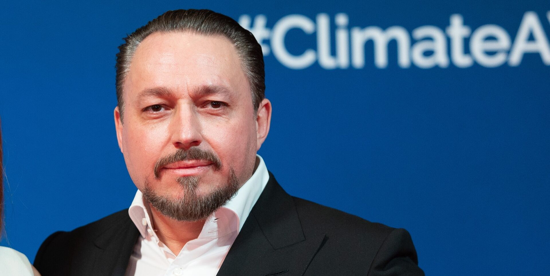 Porträt von Klemens Hallmann vor blauem Hintergrund mit „#ClimateAction“-Schriftzug, im dunklen Anzug und weißem Hemd.