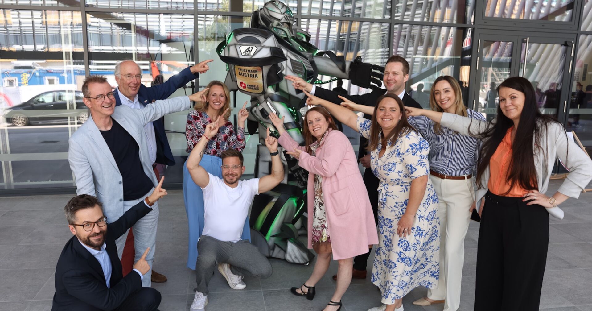 Veranstalter und Gewinner der Austrian Trustmark Awards zeigen mit ihren Fingern auf einer Roboter-Figur