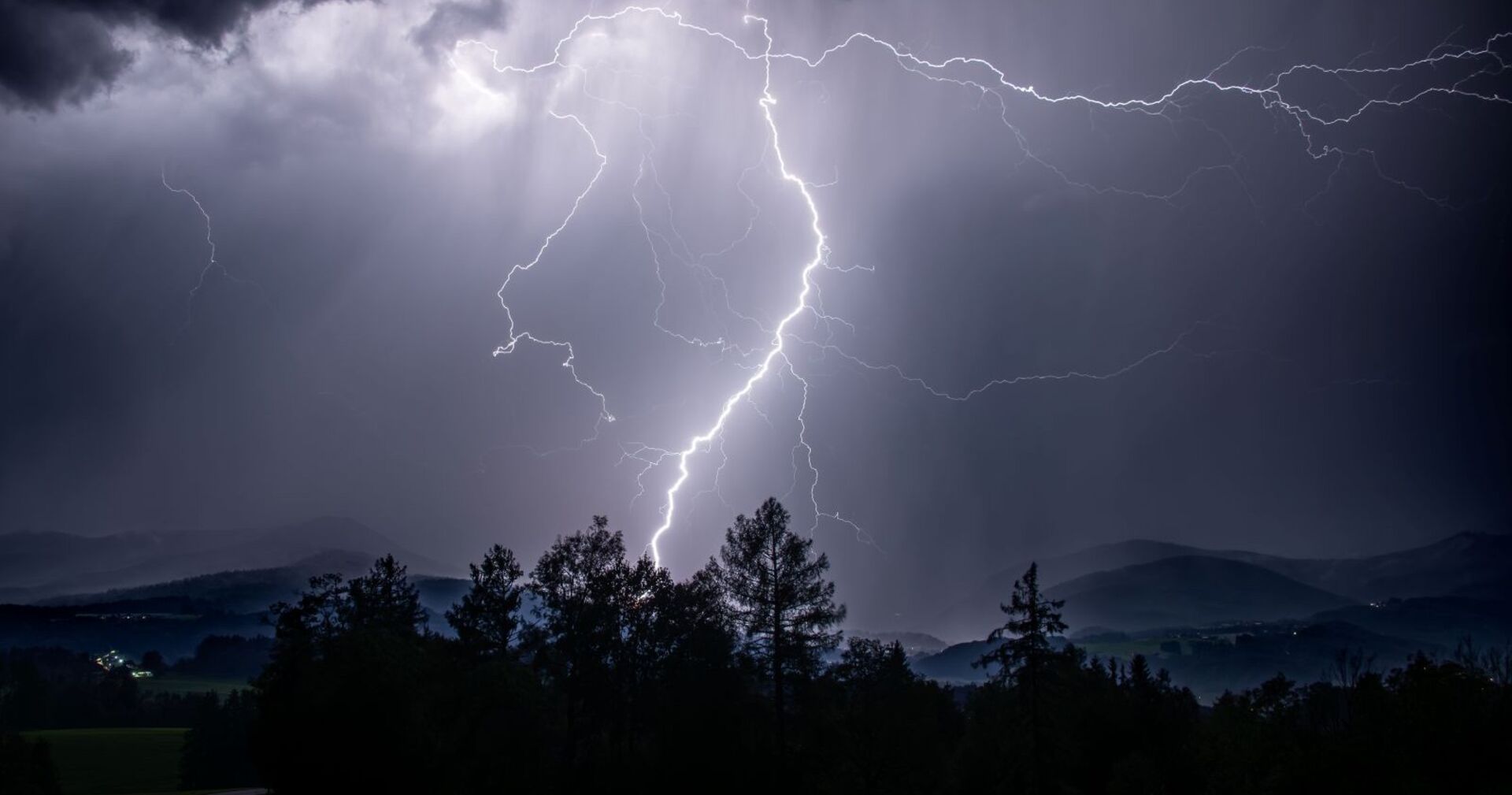Ein Gewitter mit Blitzen über einem Wald.