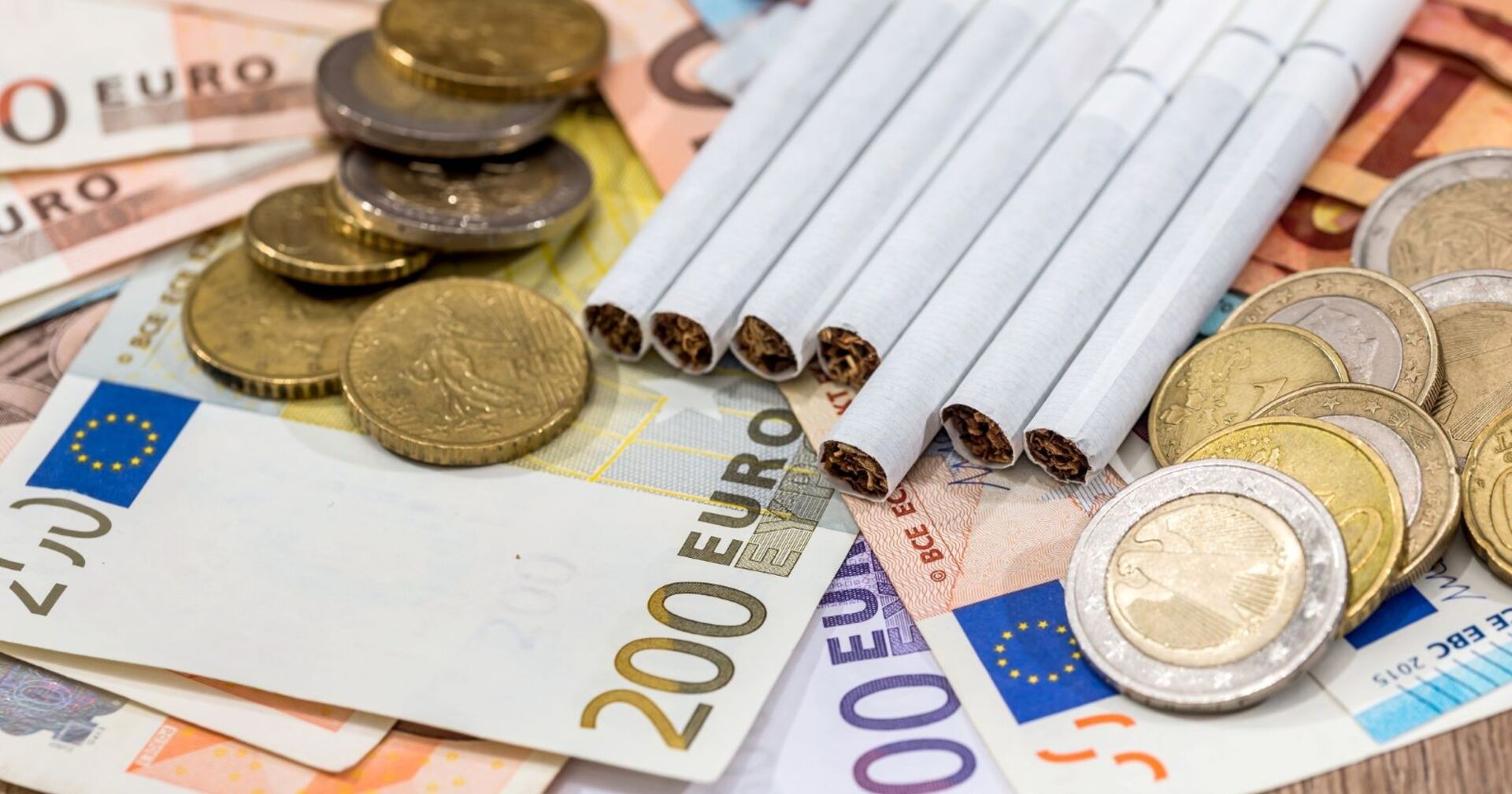 Zigaretten liegen auf Euronoten, daneben liegen Euromünzen