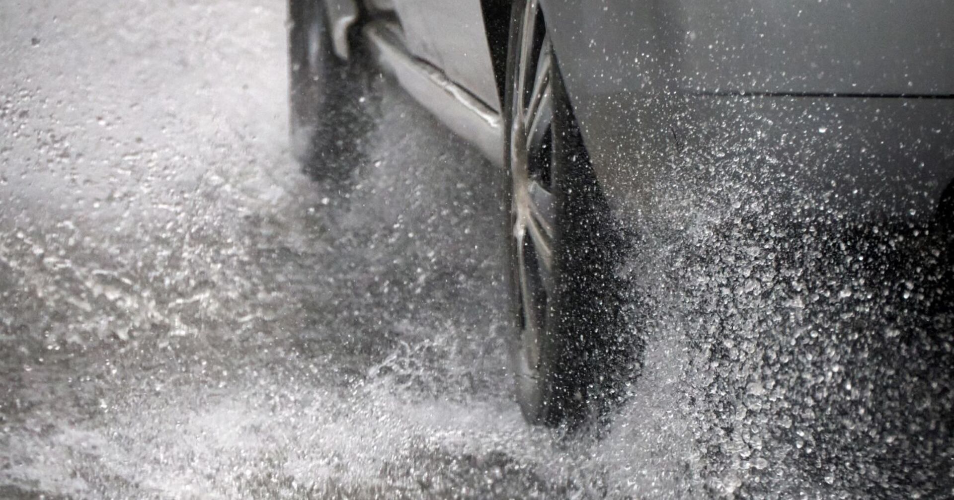 Autoreifen wirbeln Wasser auf nasser Straße auf, hohes Risiko für Aquaplaning bei starkem Regen.