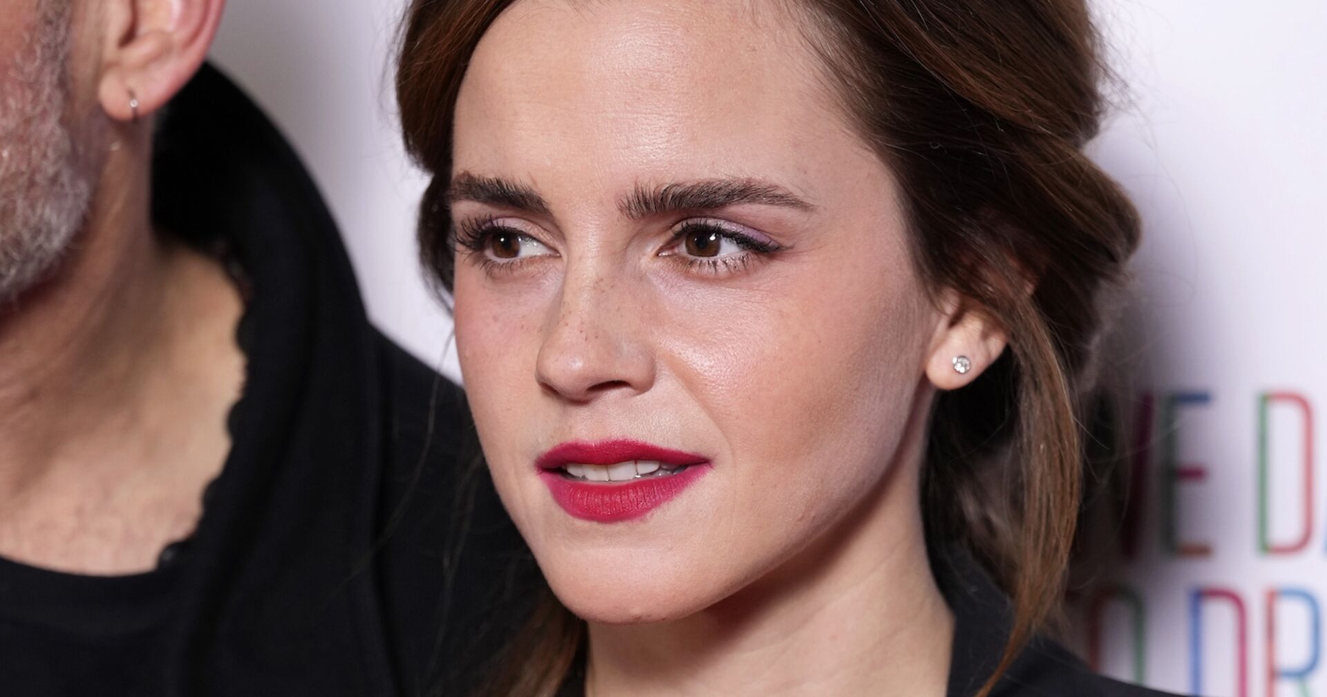 Nahaufnahme von Emma Watson mit dezentem Make-up und roten Lippen, lächelnd bei einem öffentlichen Auftritt.