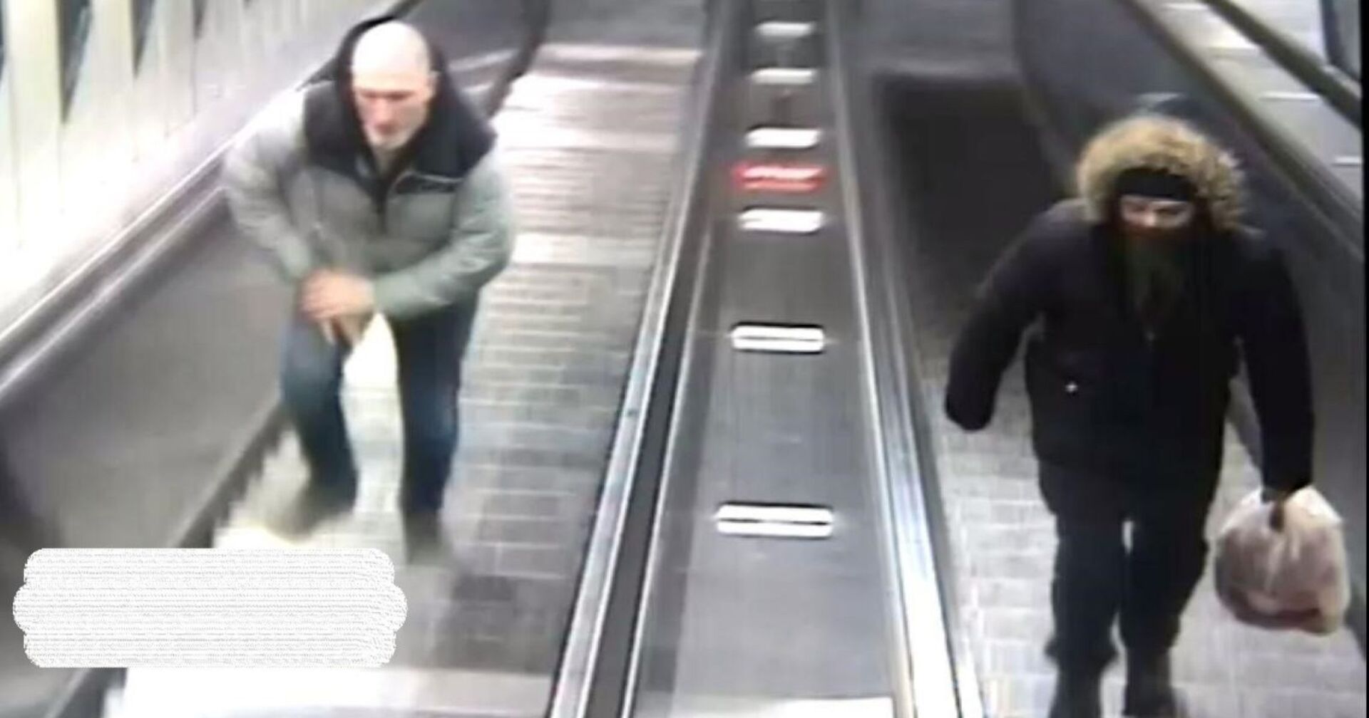 Fahndungsfoto: Zwei Männer auf Rolltreppen, links: ein Mann mit weißem Bart und dunkelgrüner Jacke, rechts: ein schwarz gekleideter, vermummter Mann mit Müllsack in der Hand und Kapuze über dem Kopf