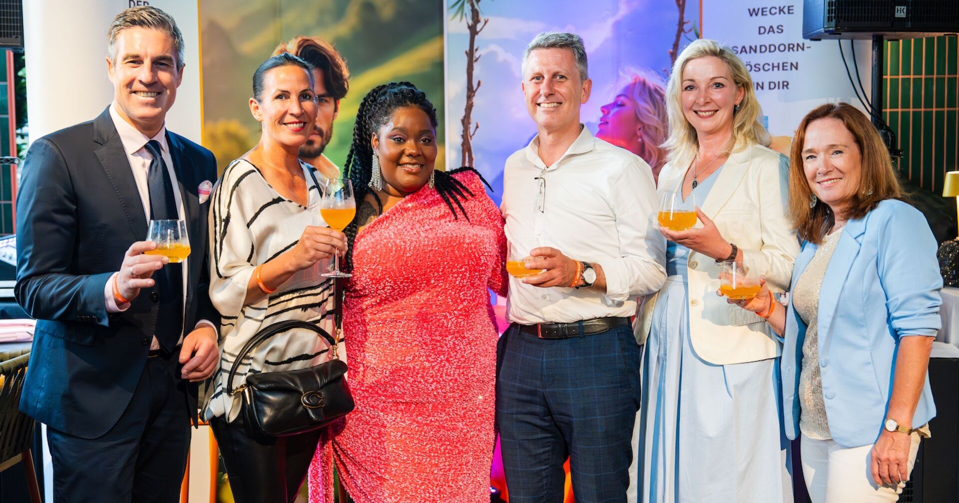 Sechs Personen lächeln mit Sommerdrink in der Hand