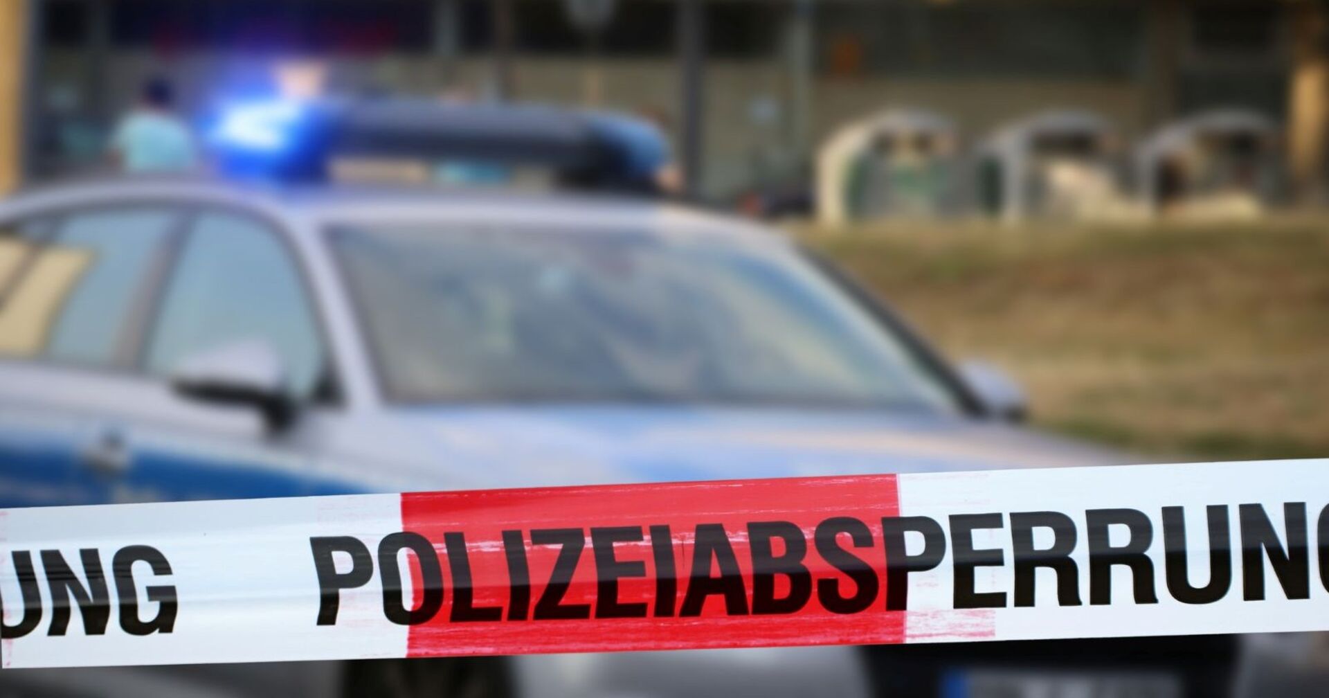 Polizeiwagen an einem Tatort, davor ist ein Polizeiabsperrband befestigt