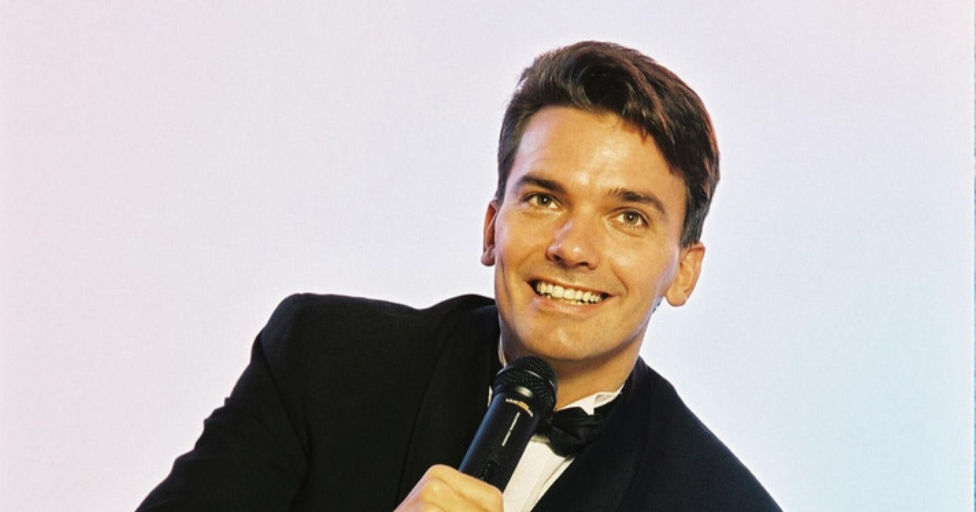 Harry Blümel im Smoking mit einem Mikrofon in seiner Hand