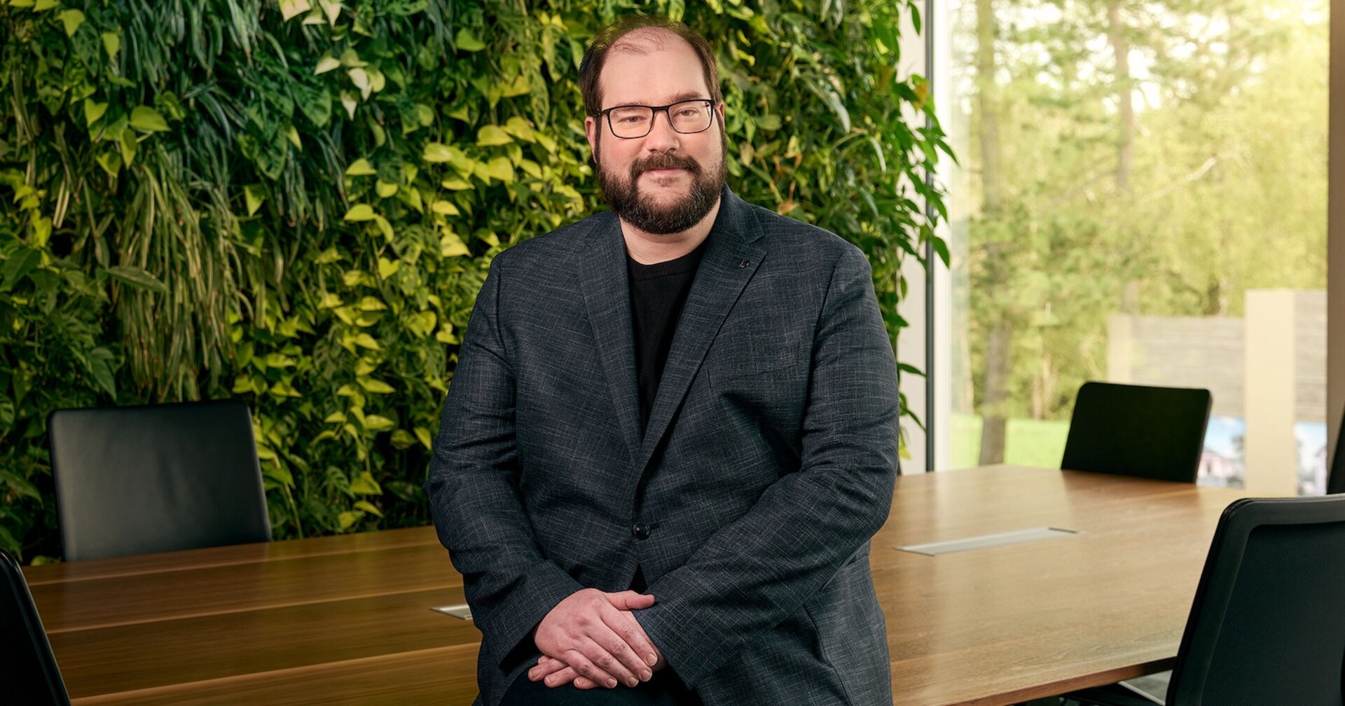 Geschäftsführer Yves Suter mit Bart und Brille vor einer grünen Pflanzenwand