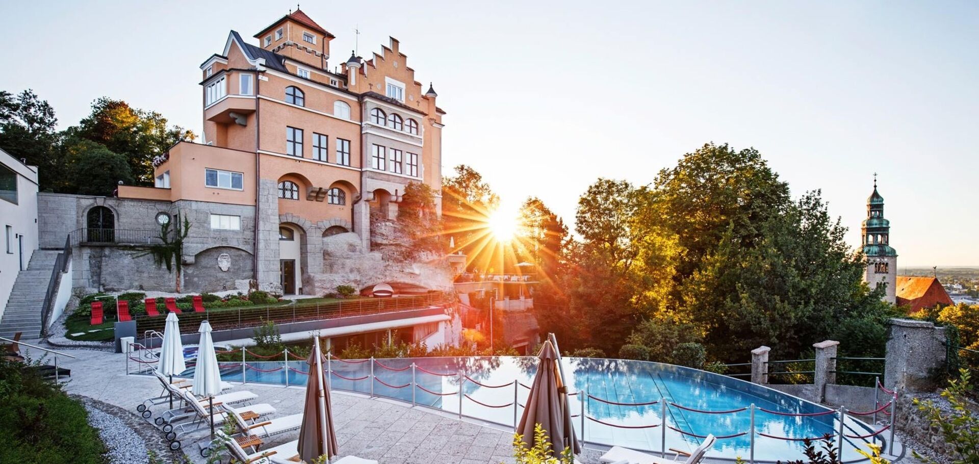 Hotel Schloss Mönchstein mit Infinity-Pool im Sonnenuntergang, Blick auf die Stadt Salzburg und den Mönchsberg