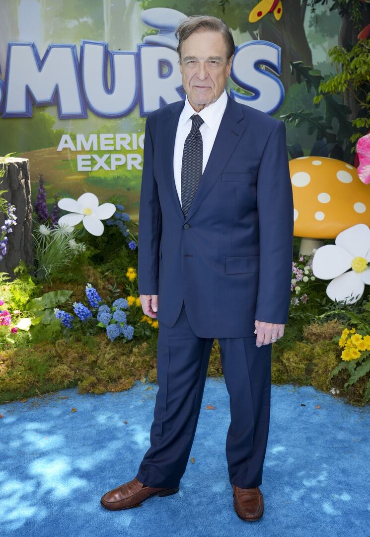 „John Goodman schlank im dunkelblauen Anzug auf dem blauen Teppich bei der Premiere des neuen ‚Smurfs‘-Films.“