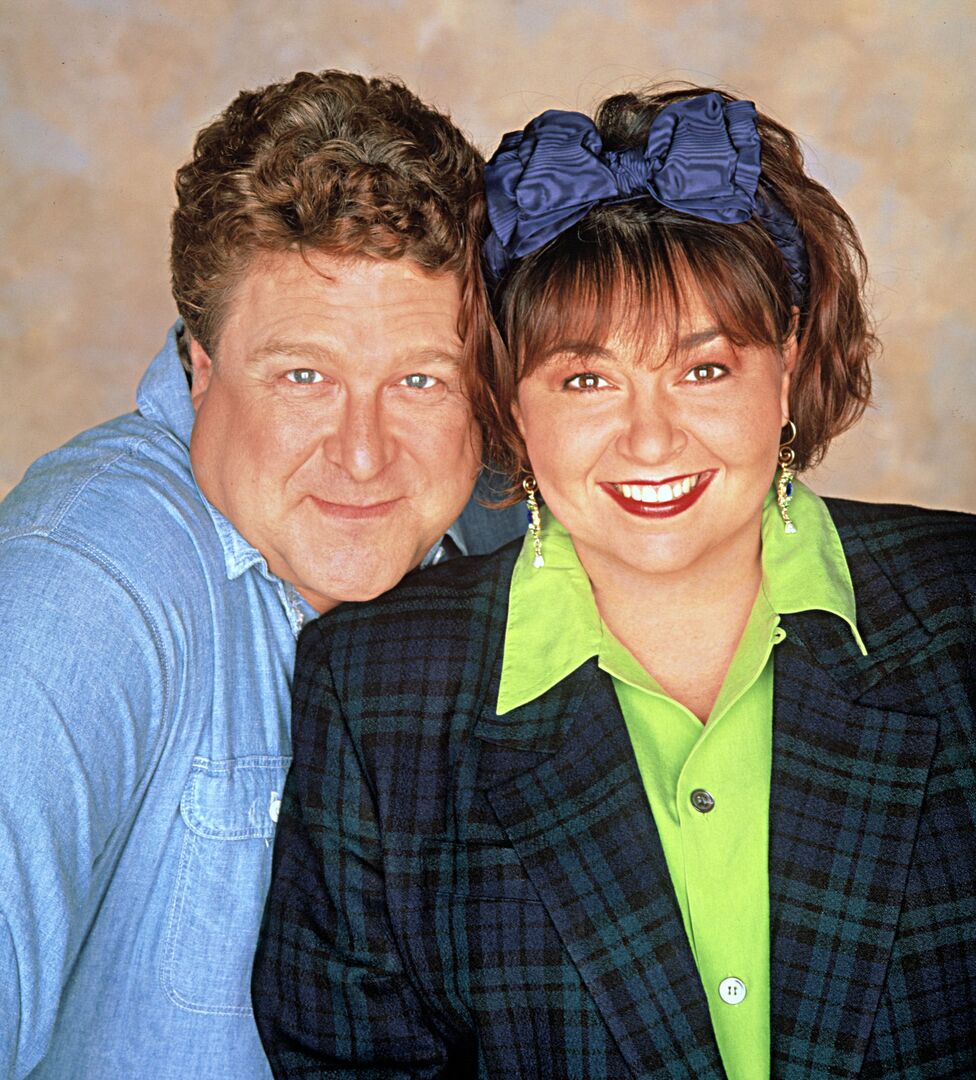 John Goodman und Roseanne Barr lächelnd nebeneinander in einer Promofotoaufnahme zur Serie ‚Roseanne‘.“