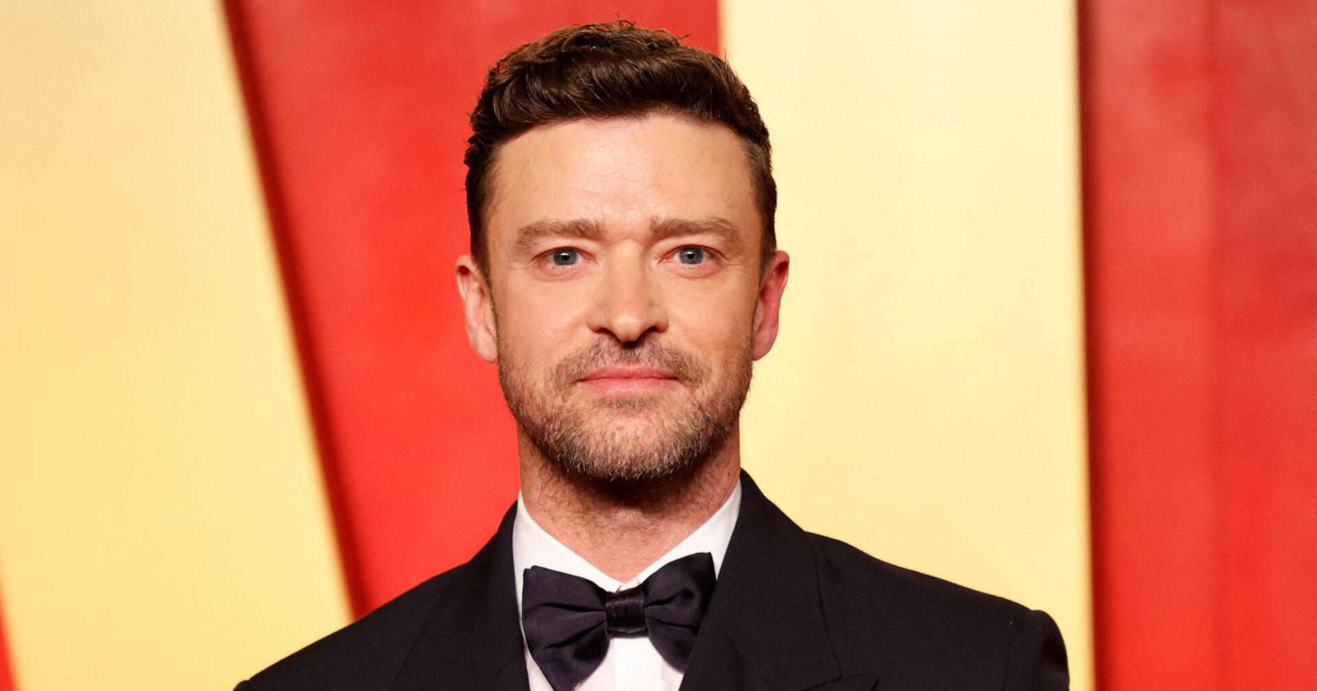 Justin Timberlake im Anzug mit Fliege vor gelb-rot-gestreiftem Hintergrund