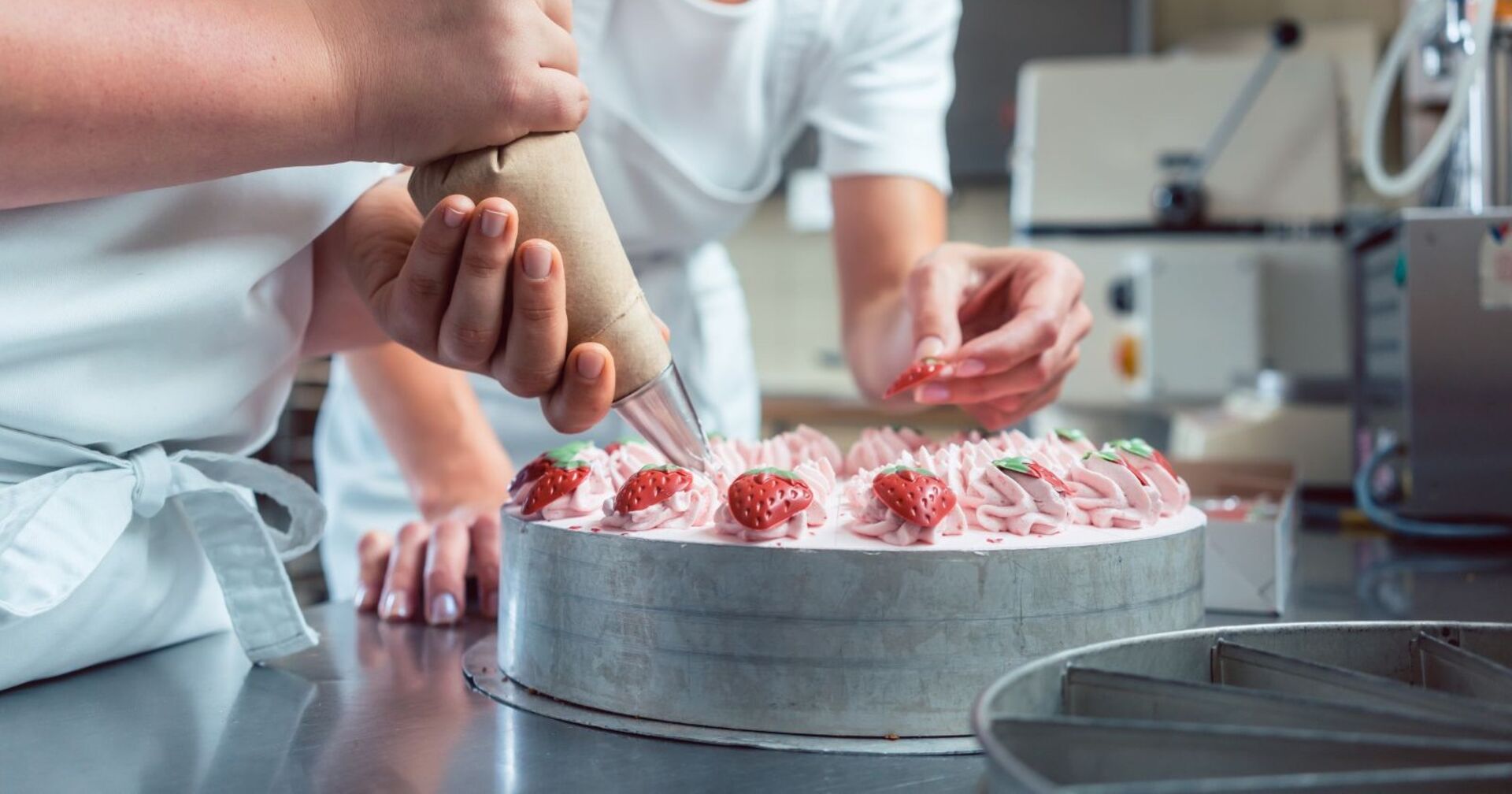 Konditoren mit Spritzbeutel in der Hand beim Verzieren einer Erdbeertorte