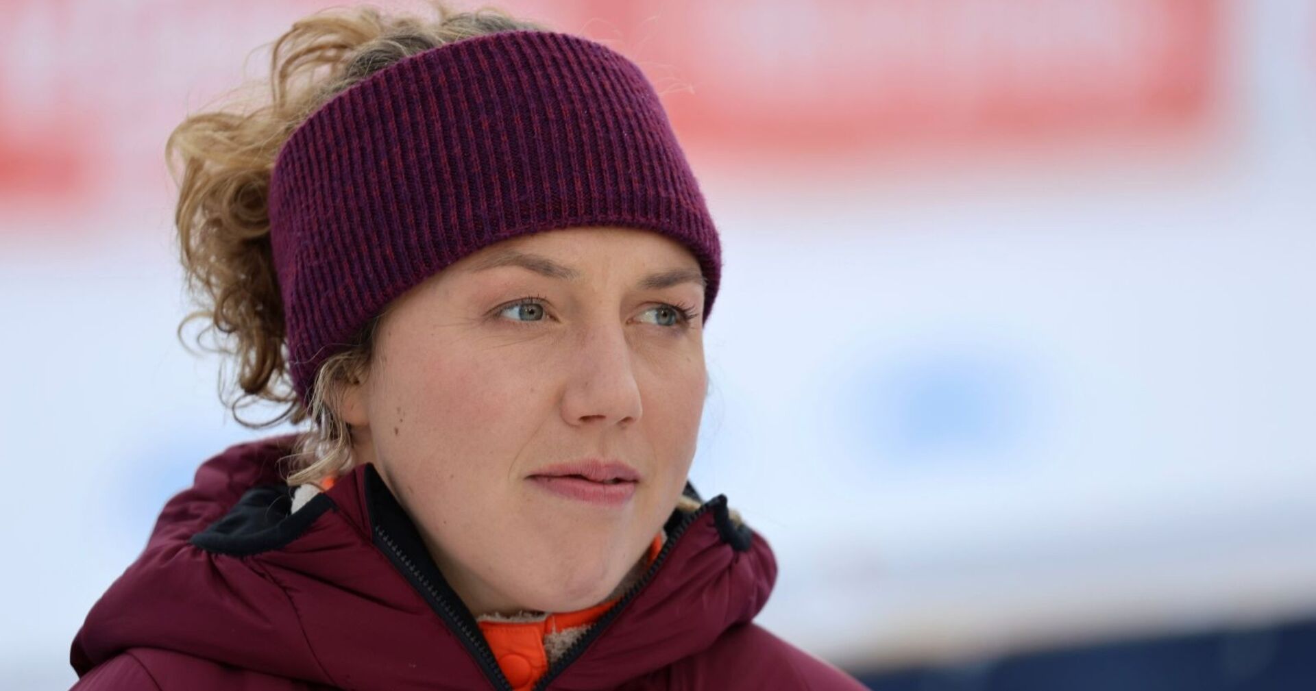 Nahaufnahme von Laura Dahlmeier mit violettem Stirnband und roter Winterjacke, aufgenommen bei einer Veranstaltung im Freien.