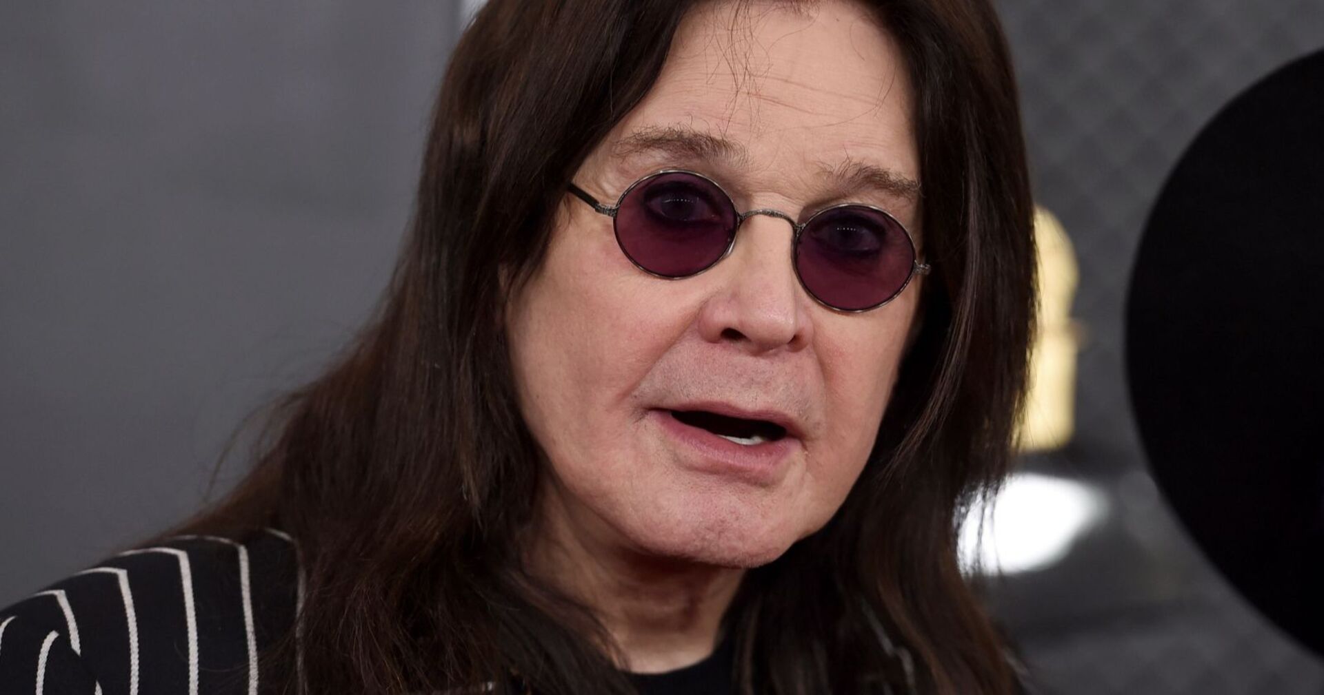Porträt von Ozzy Osbourne mit langen dunklen Haaren und runder Sonnenbrille, aufgenommen bei einem öffentlichen Auftritt.
